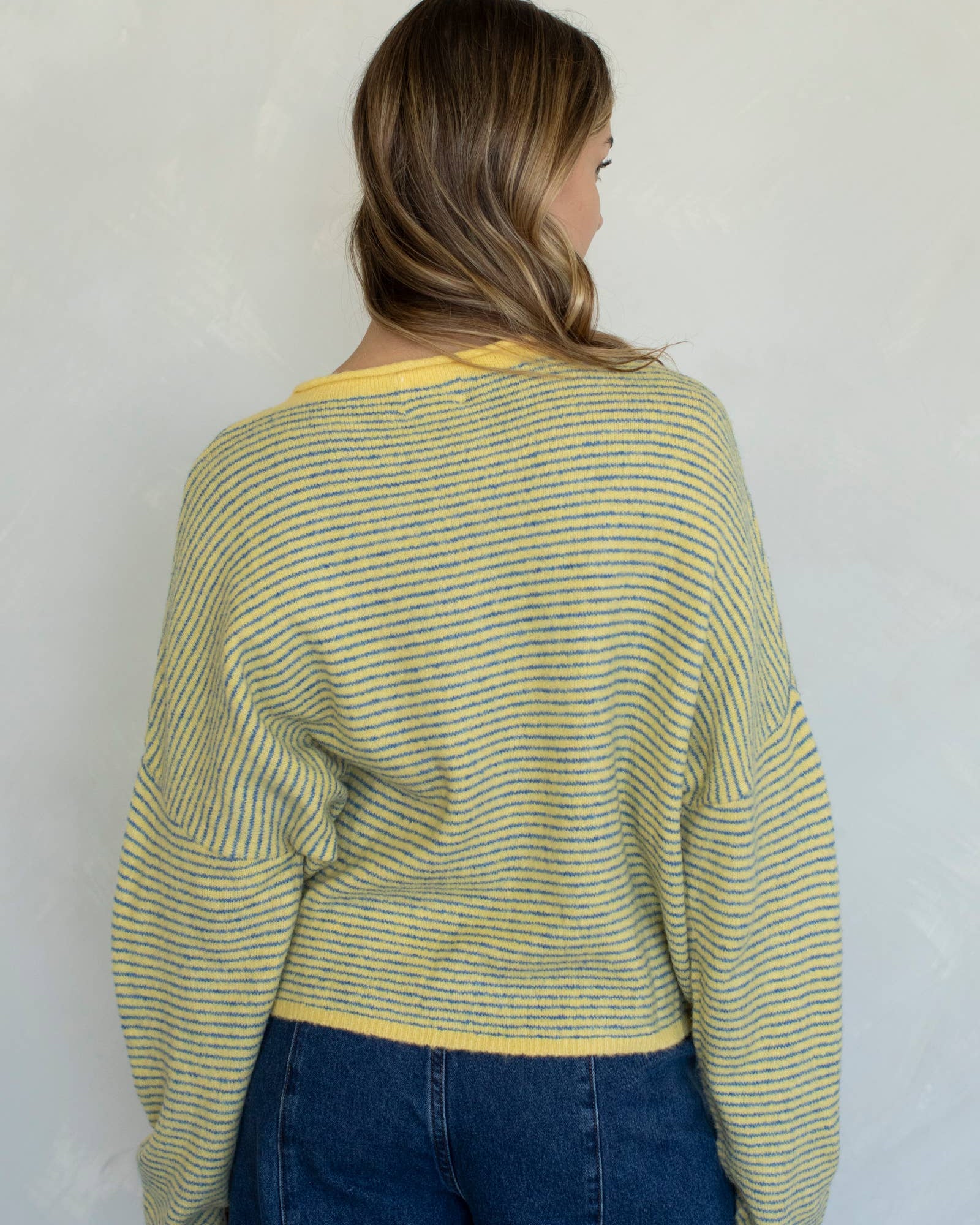 Woman wearing a green and yellow striped sweater against a white wall