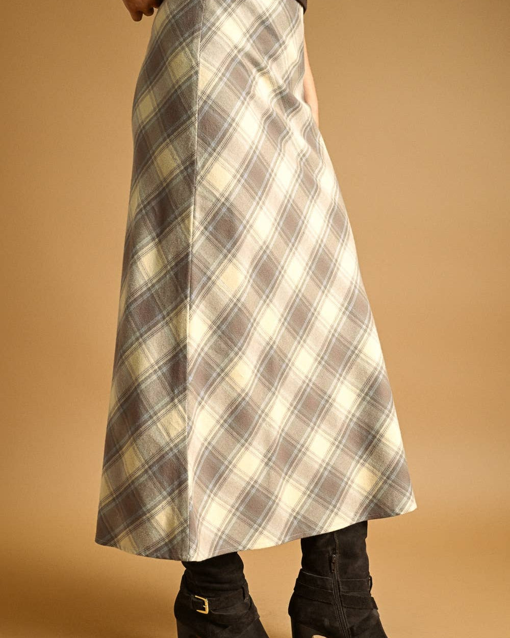 Person wearing a plaid skirt and black boots on a beige background