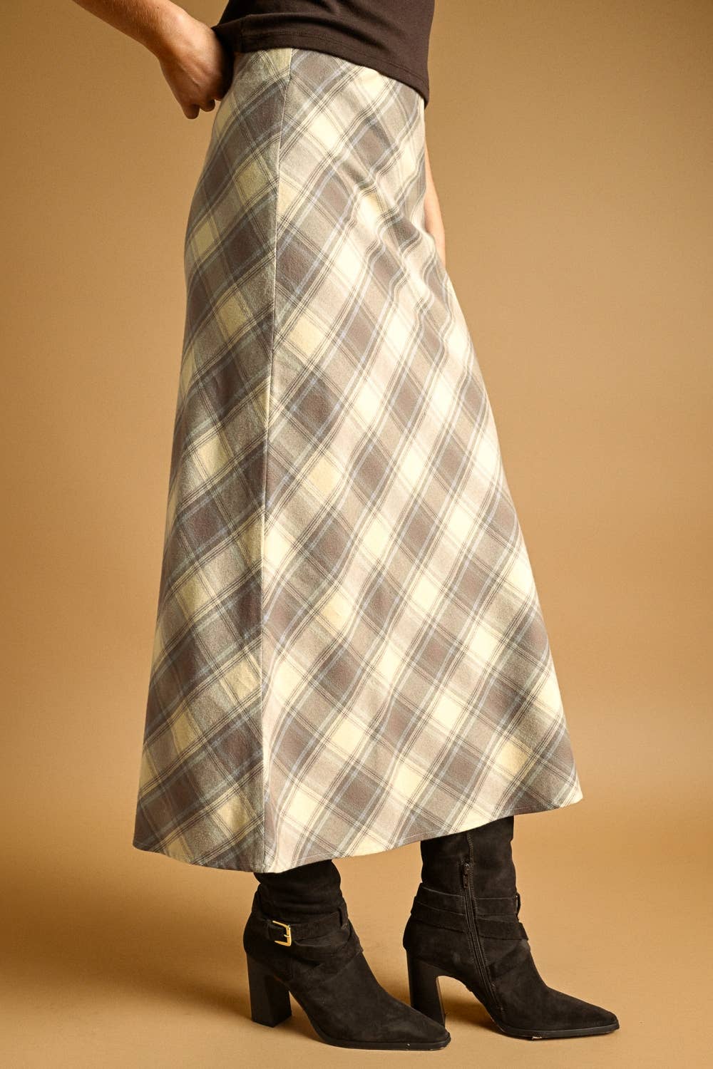 Person wearing a plaid skirt and black boots on a beige background