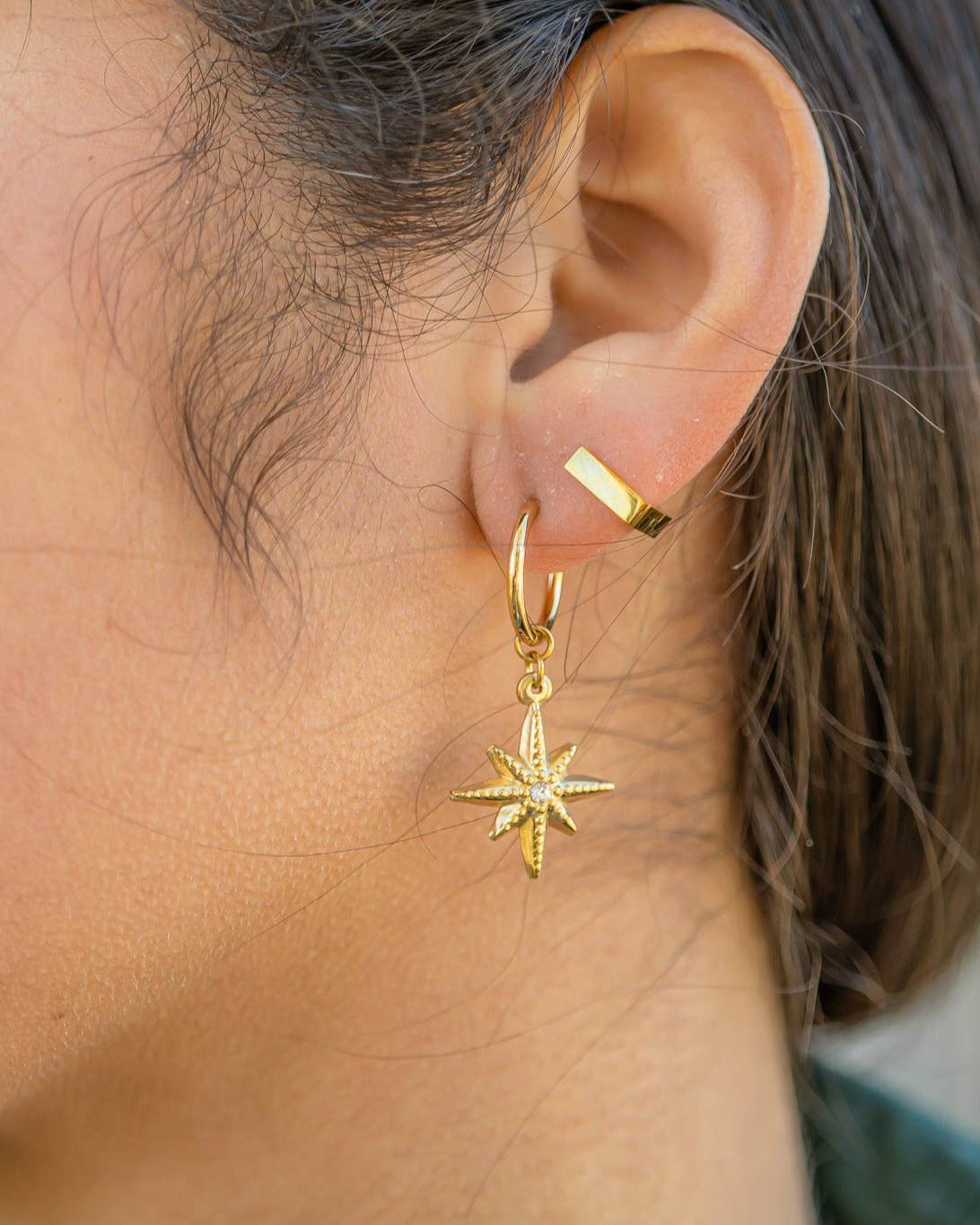 Close-up of a person wearing a gold hoop earring with a star-shaped pendant.