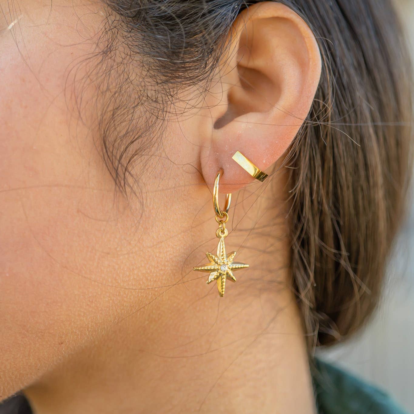 Close-up of a person wearing a gold hoop earring with a star-shaped pendant.