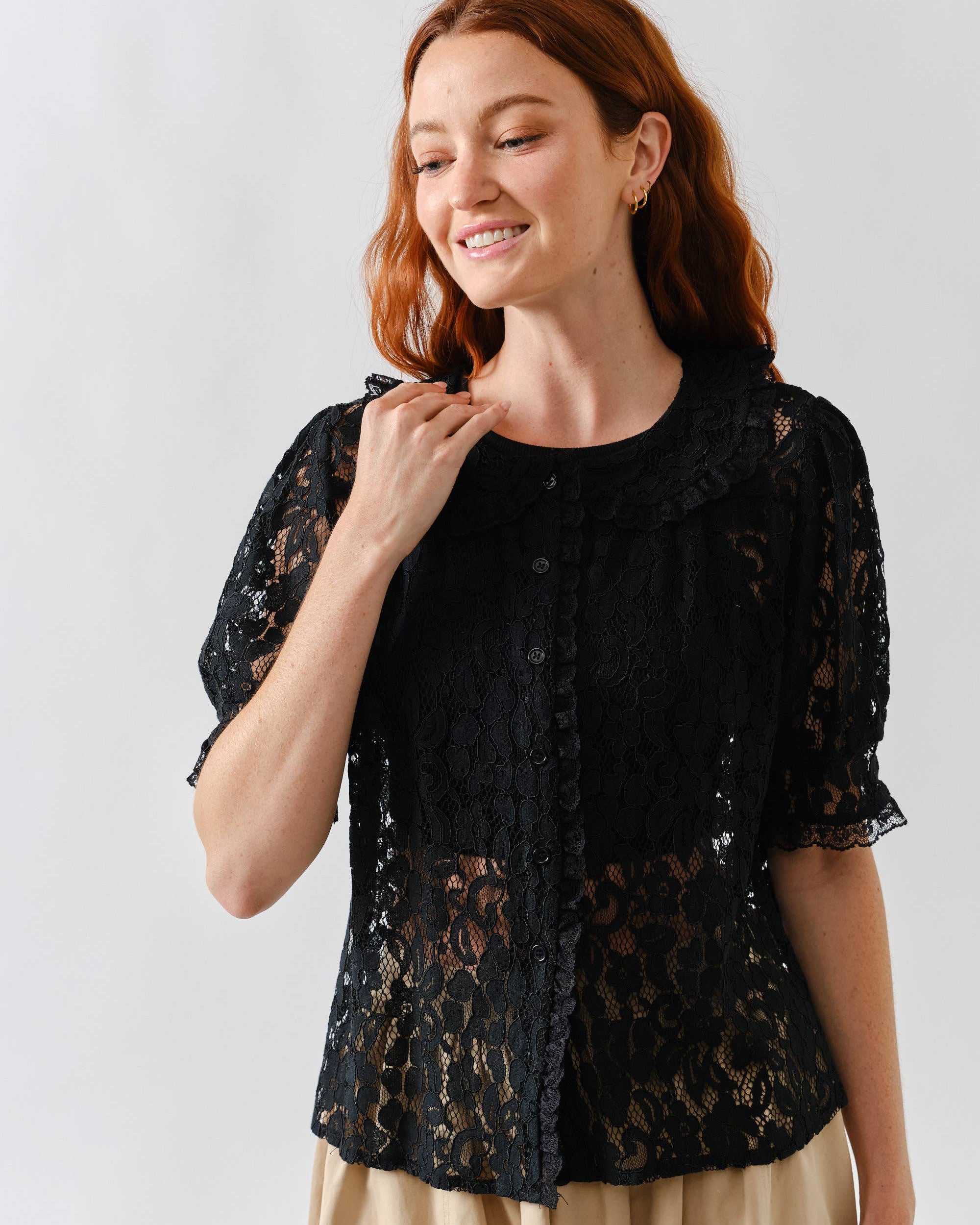 Woman wearing black lace button up blouse with beige bottoms