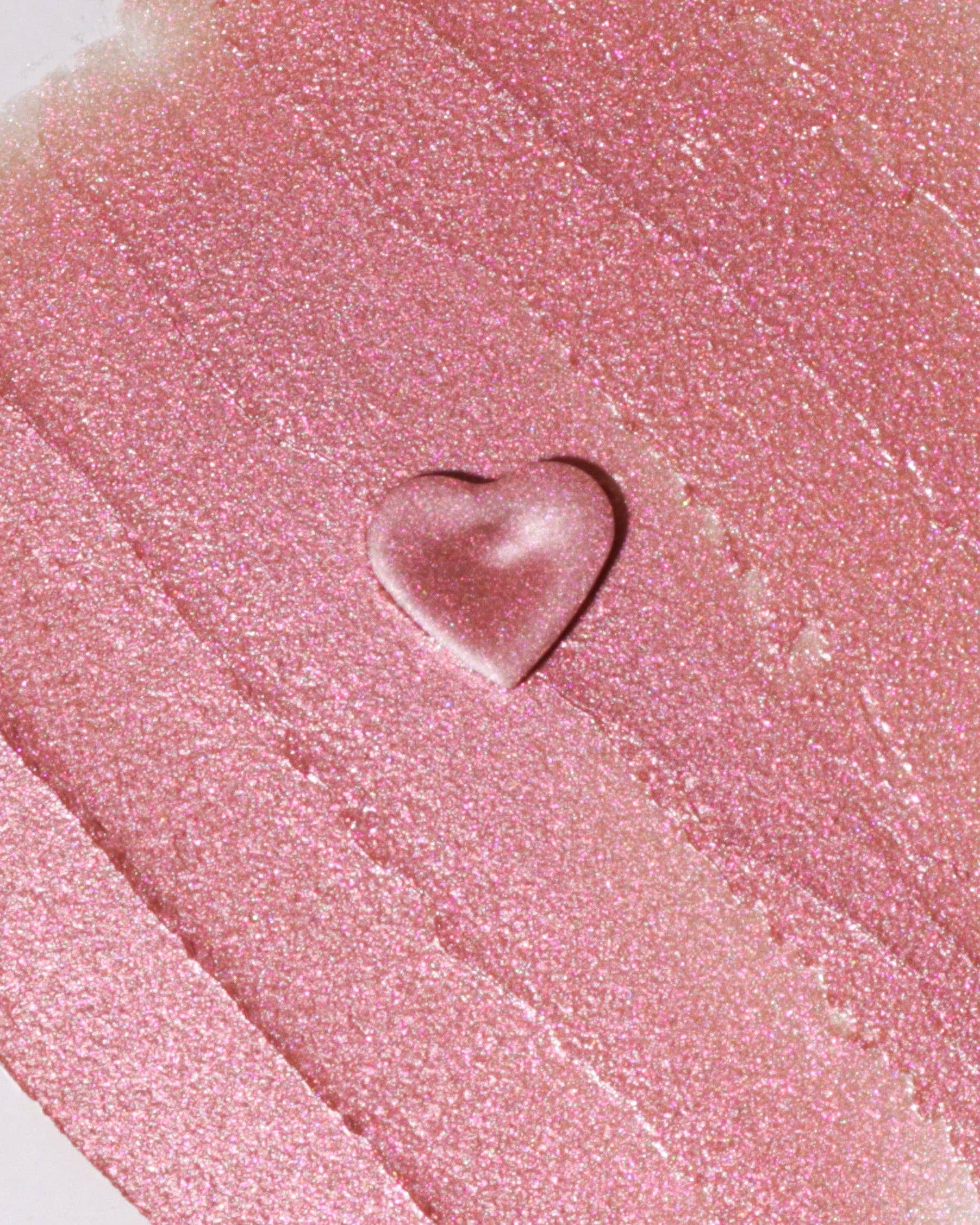 Close-up of pink lip gloss with a heart-shaped droplet on a textured surface