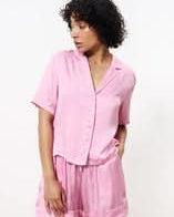 Woman wearing pink short sleeve cropped satin blouse with boxy shape with collar revere, v neck and ivory buttons.