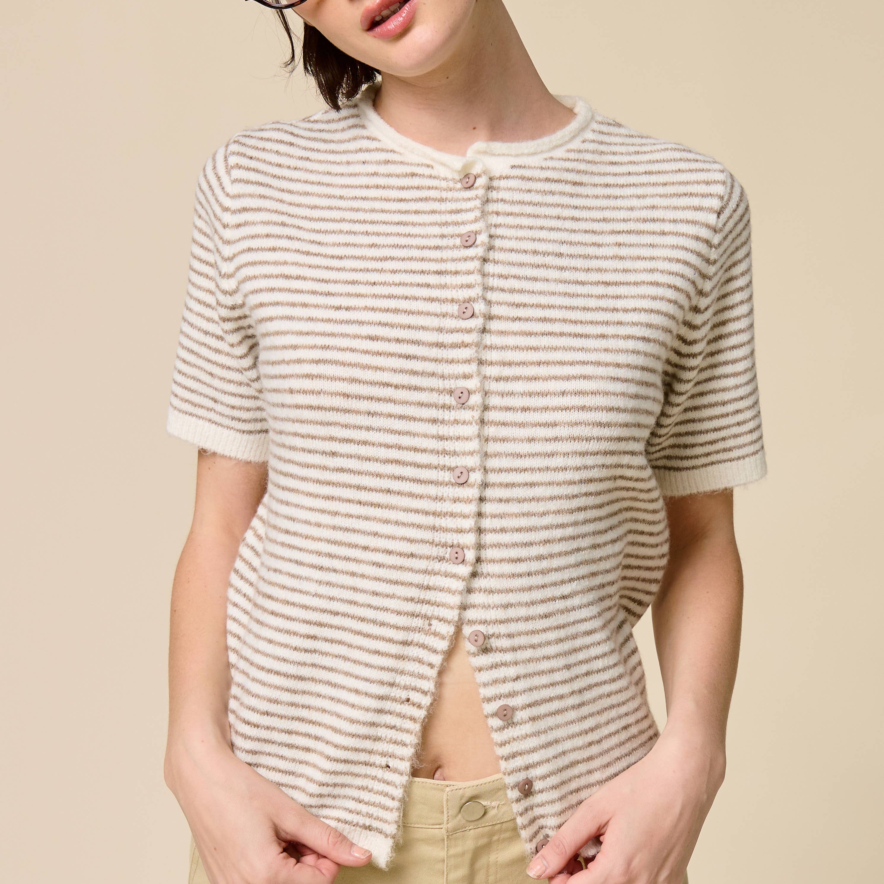 Person wearing a striped shirt, beige cap, and glasses on a beige background