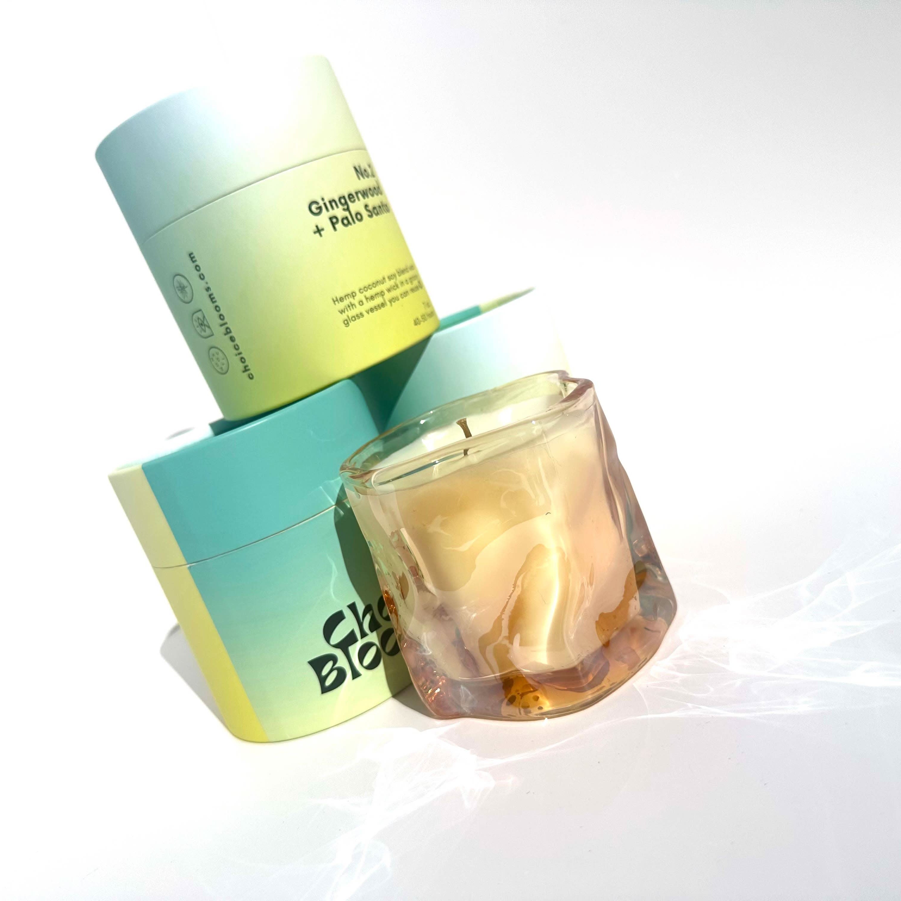 One candle in tinted pink wavy glass container next to three Aqua and green candle packaging containers