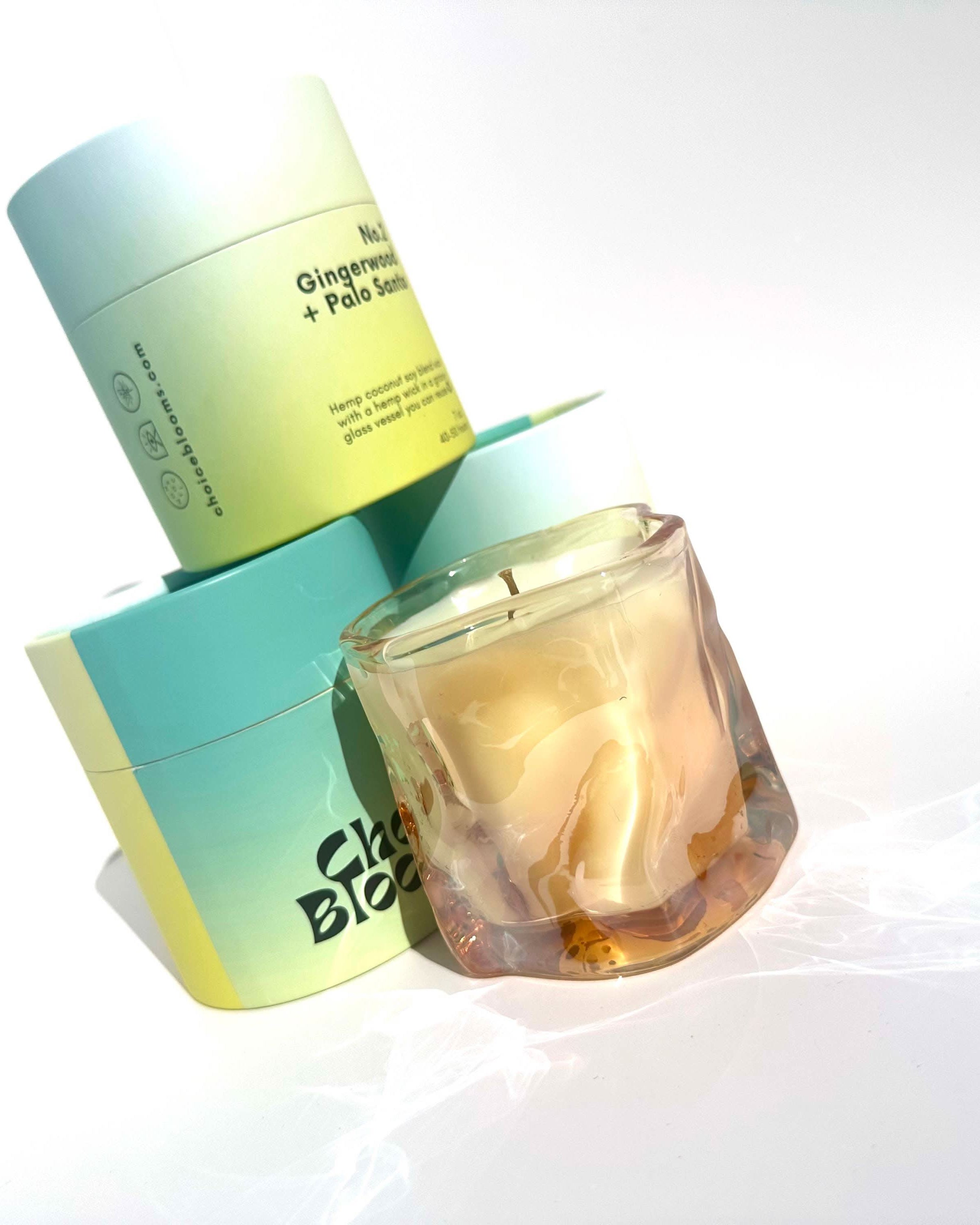 One candle in tinted pink wavy glass container next to three Aqua and green candle packaging containers