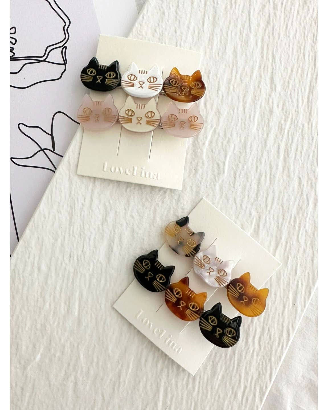 Two pairs of three colorful cats on a clip in a pack of two behind a white and purple background.