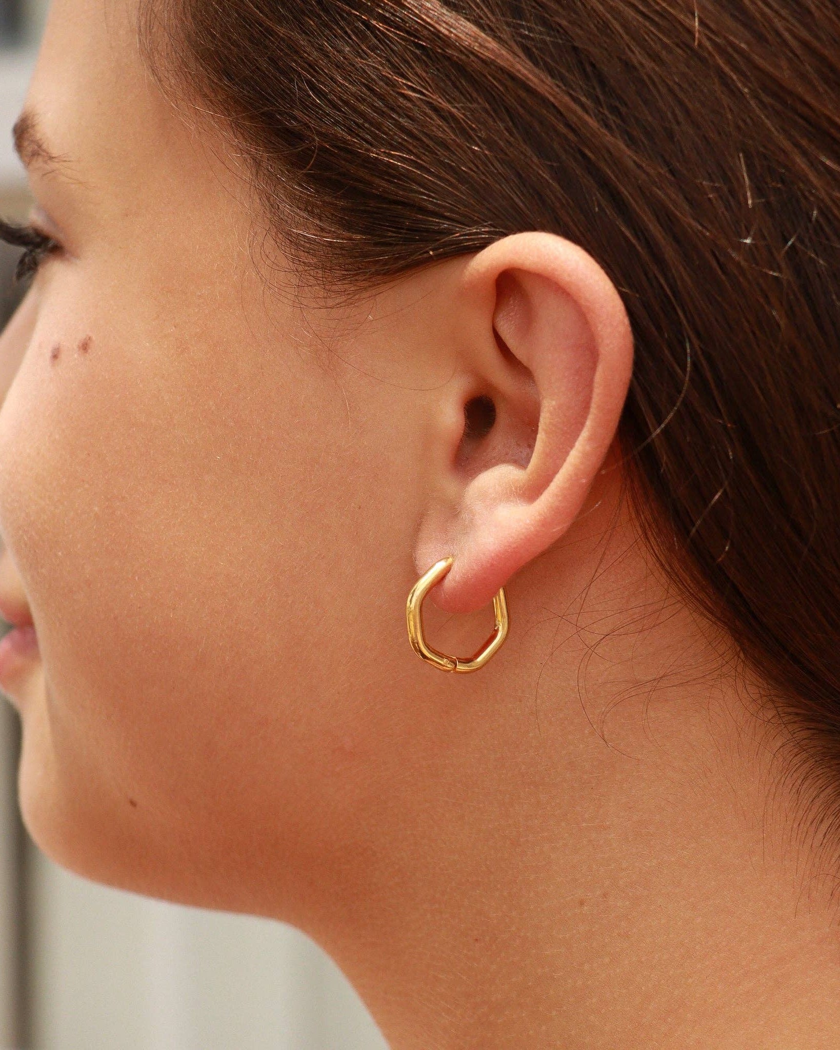 Close-up of a person wearing a gold hoop earring.