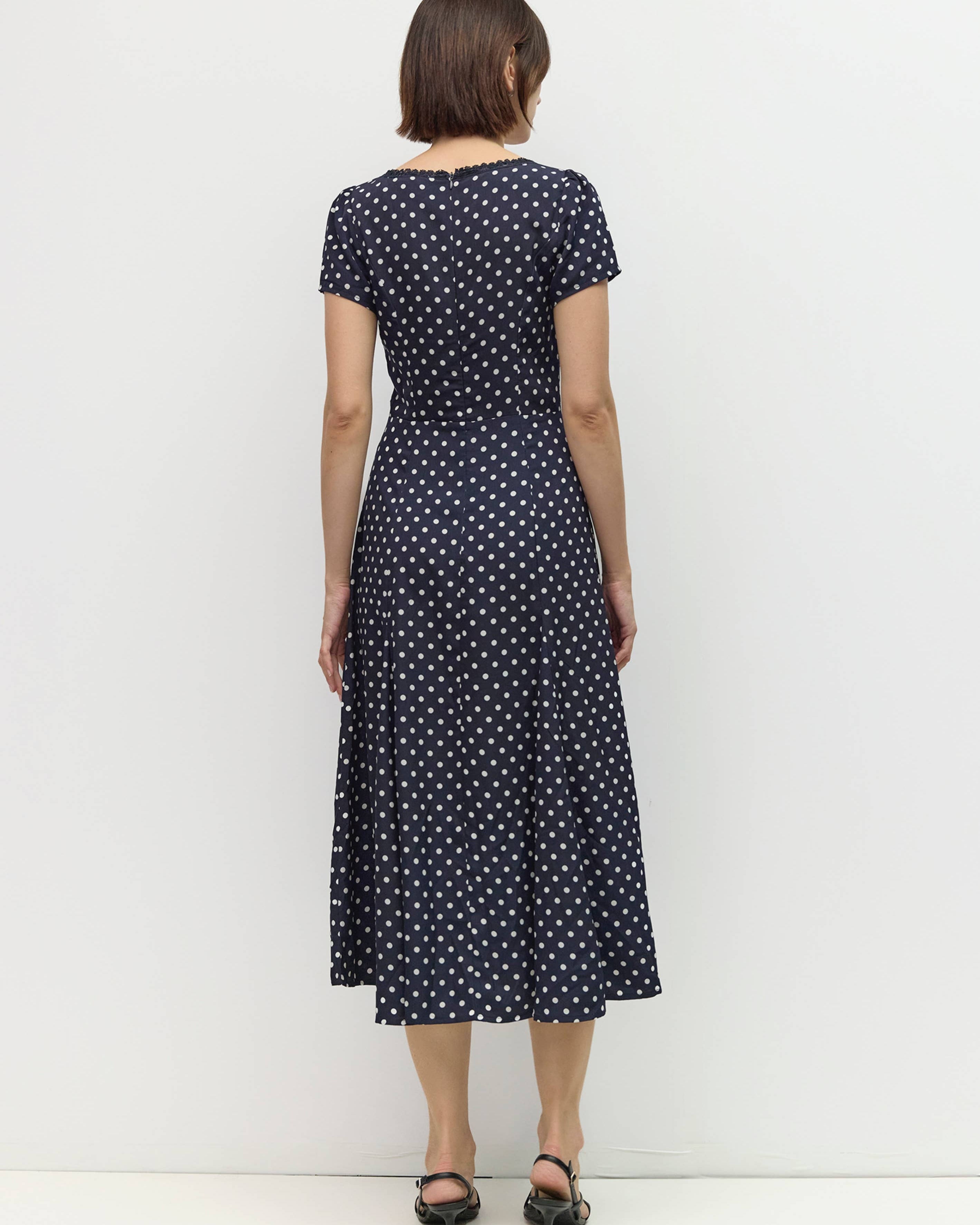 Woman wearing a navy dress with white polka dots against a white background