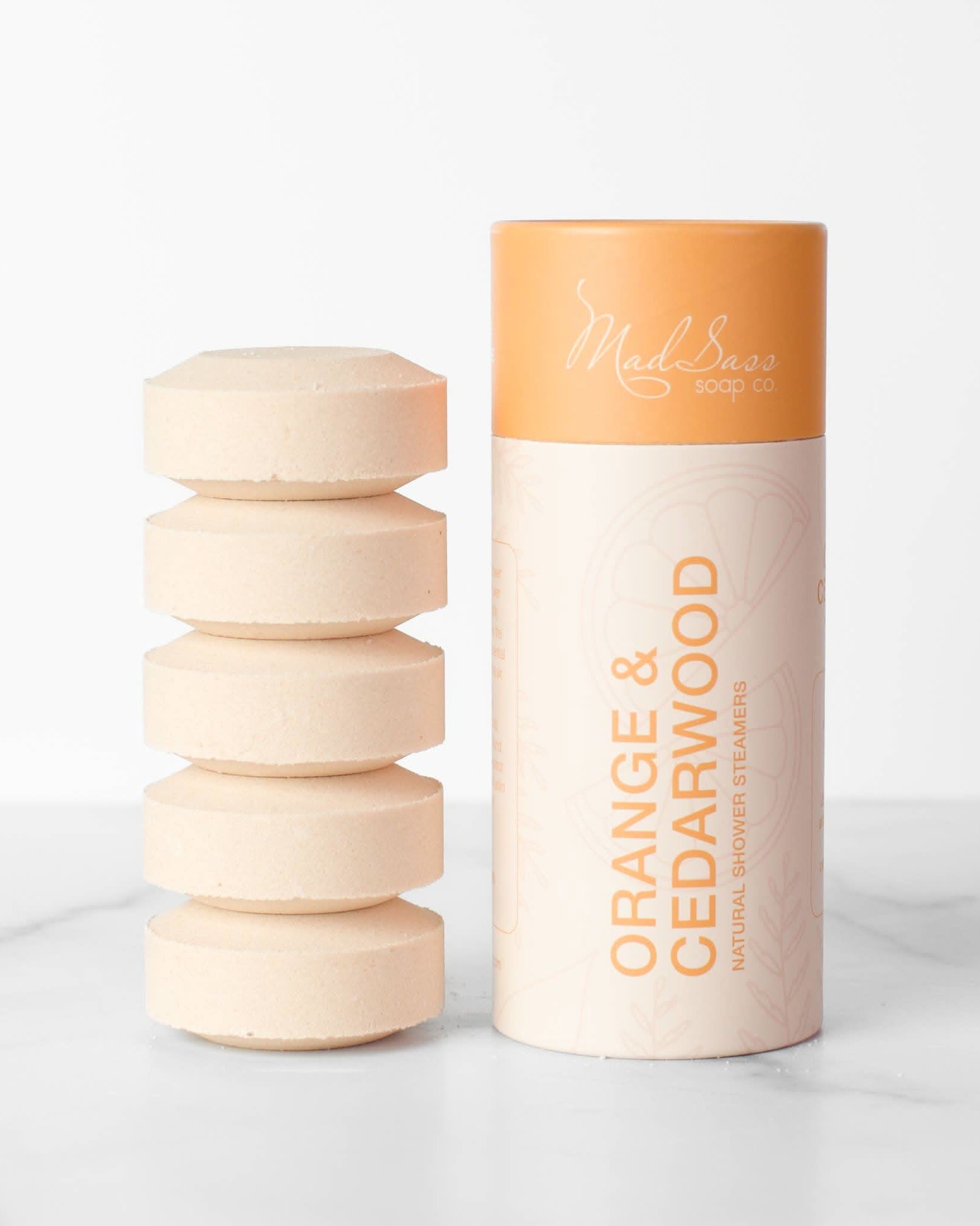 Stacked orange cedar wood shower steamer tablets next to packaging