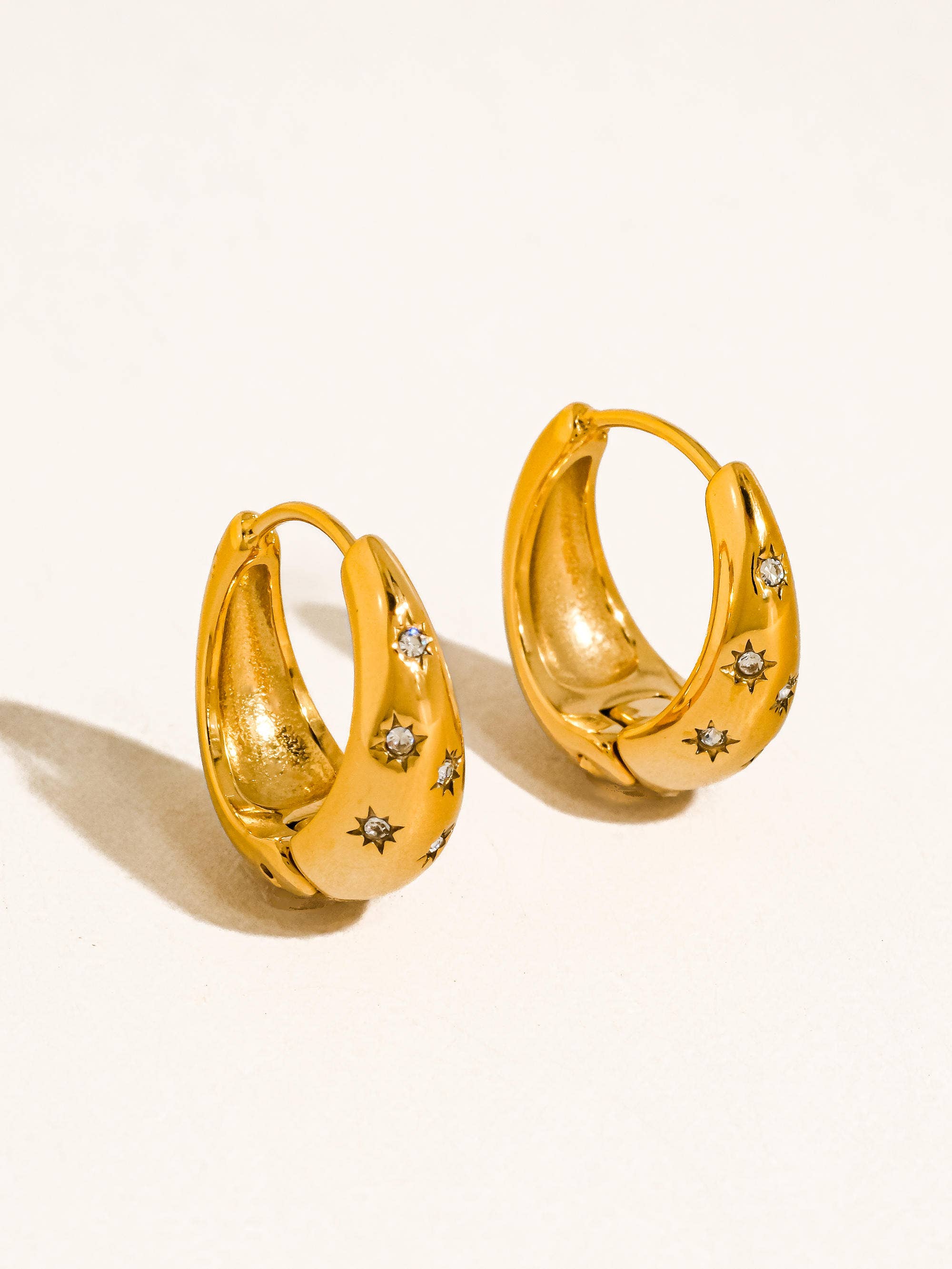 Gold hoop earrings with star designs on a beige background