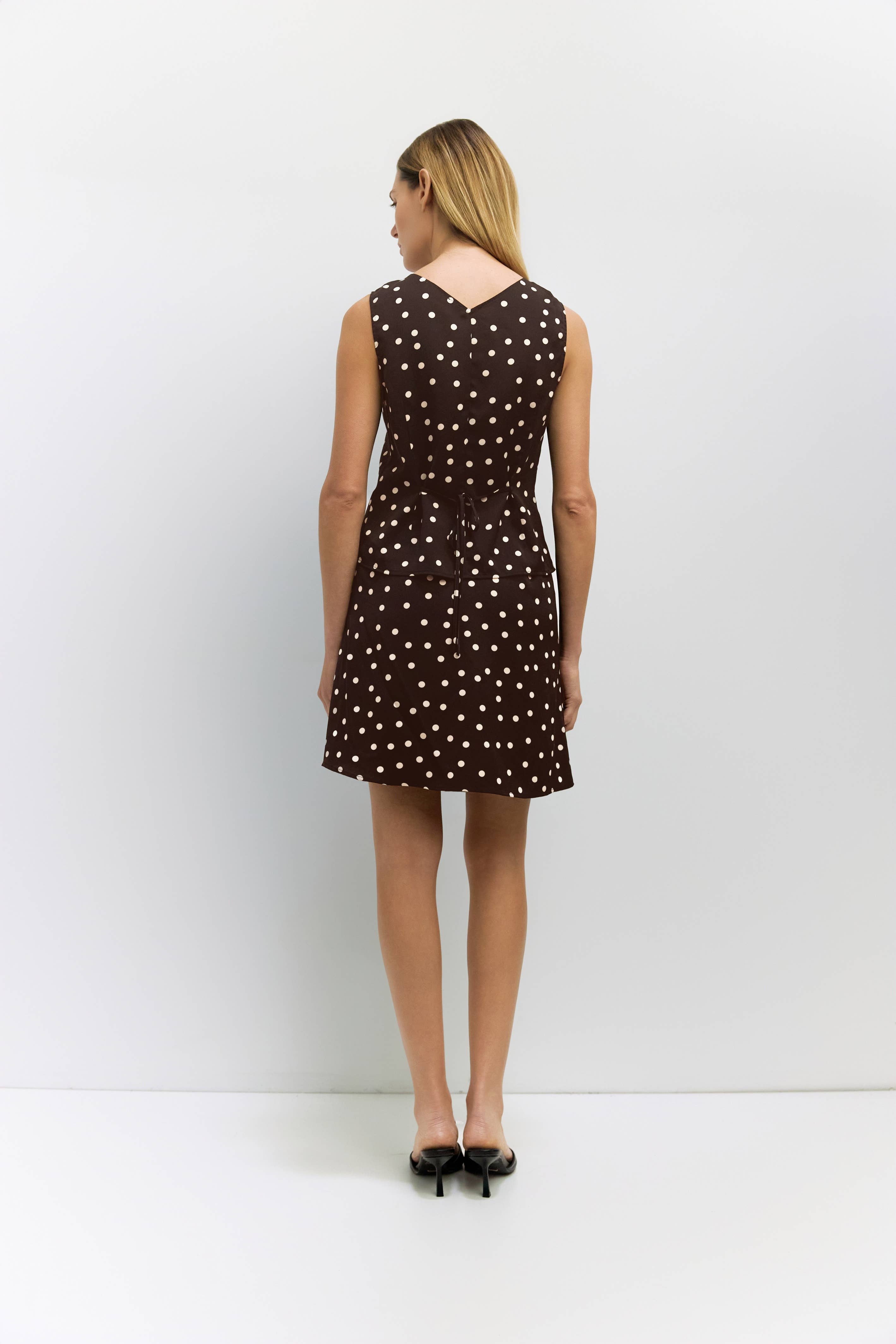 Woman wearing a brown top and skirt with white polka dots against a white background