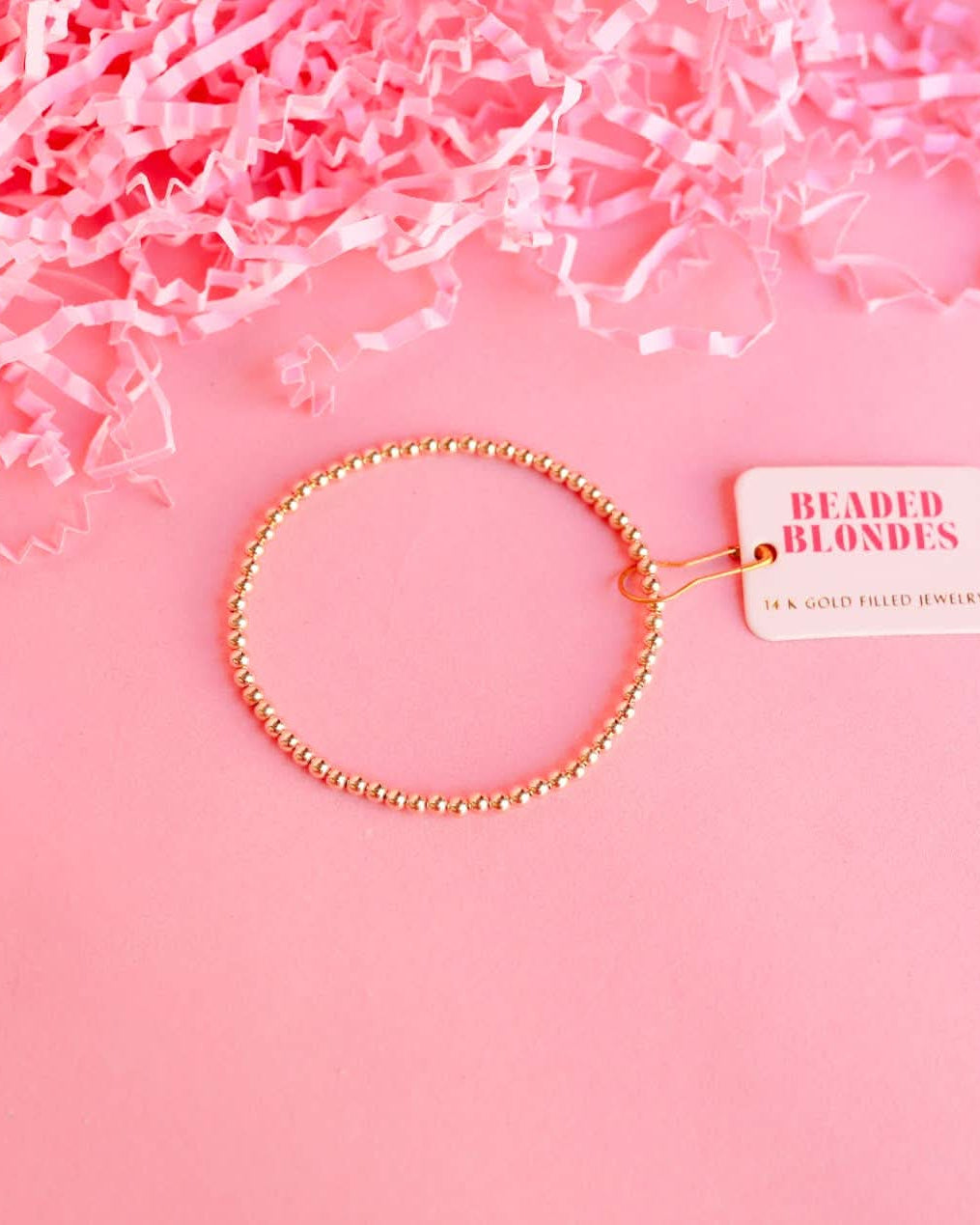 Gold beaded bracelet on a pink background with 'Beaded Blondes' tag