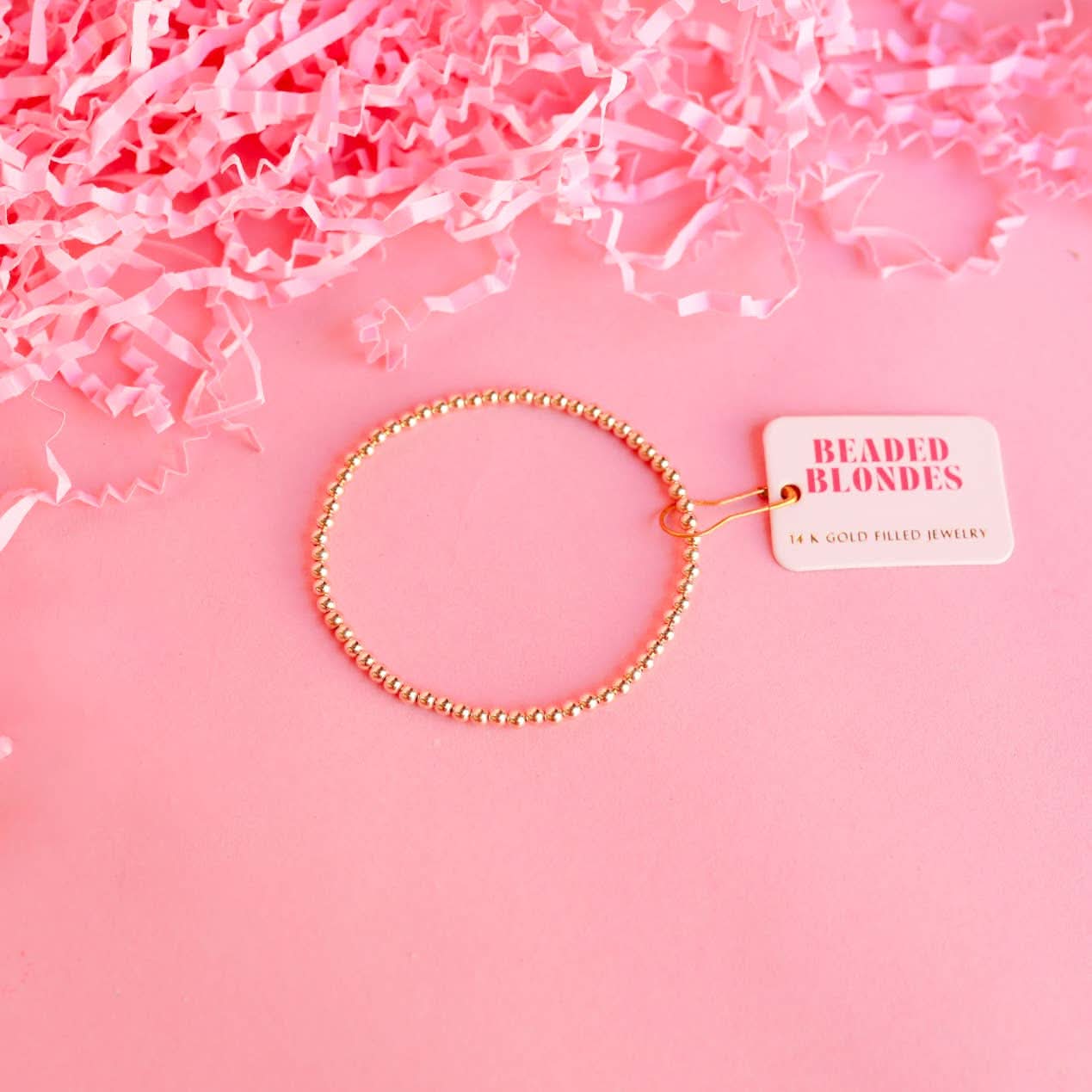 Gold beaded bracelet on a pink background with 'Beaded Blondes' tag