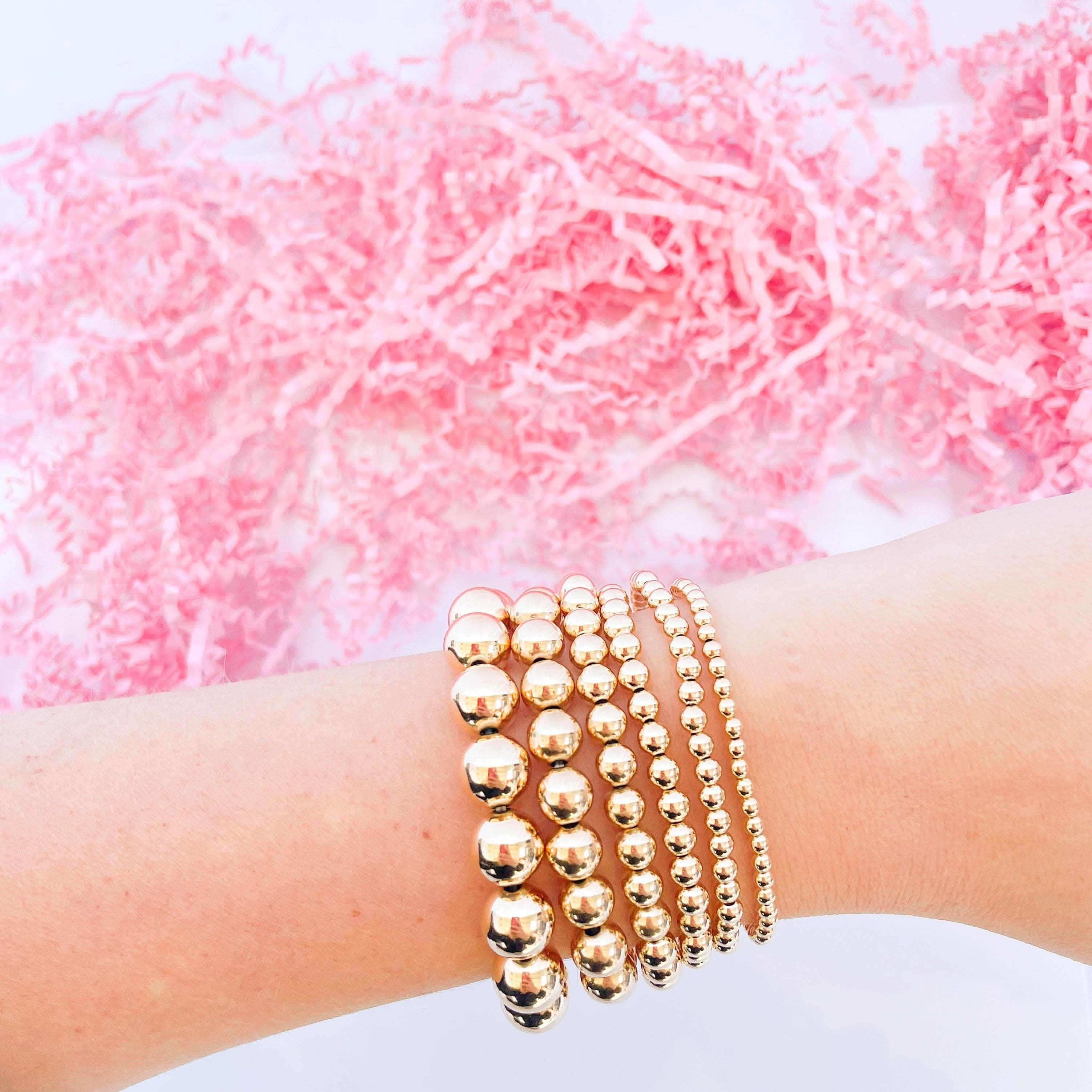 Gold beaded bracelets on a wrist with a pink textured background