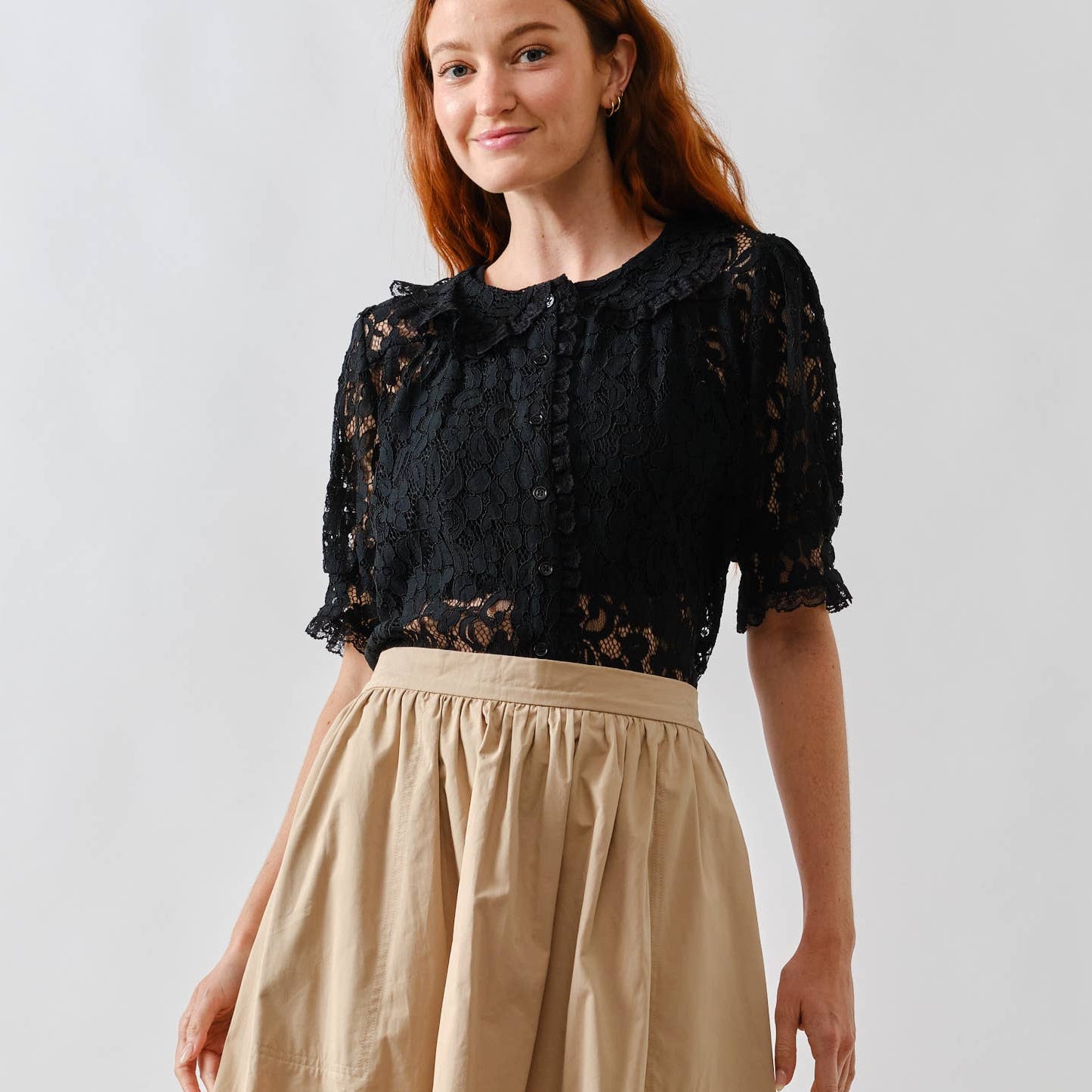 Woman wearing a black lace top and beige skirt on a white background