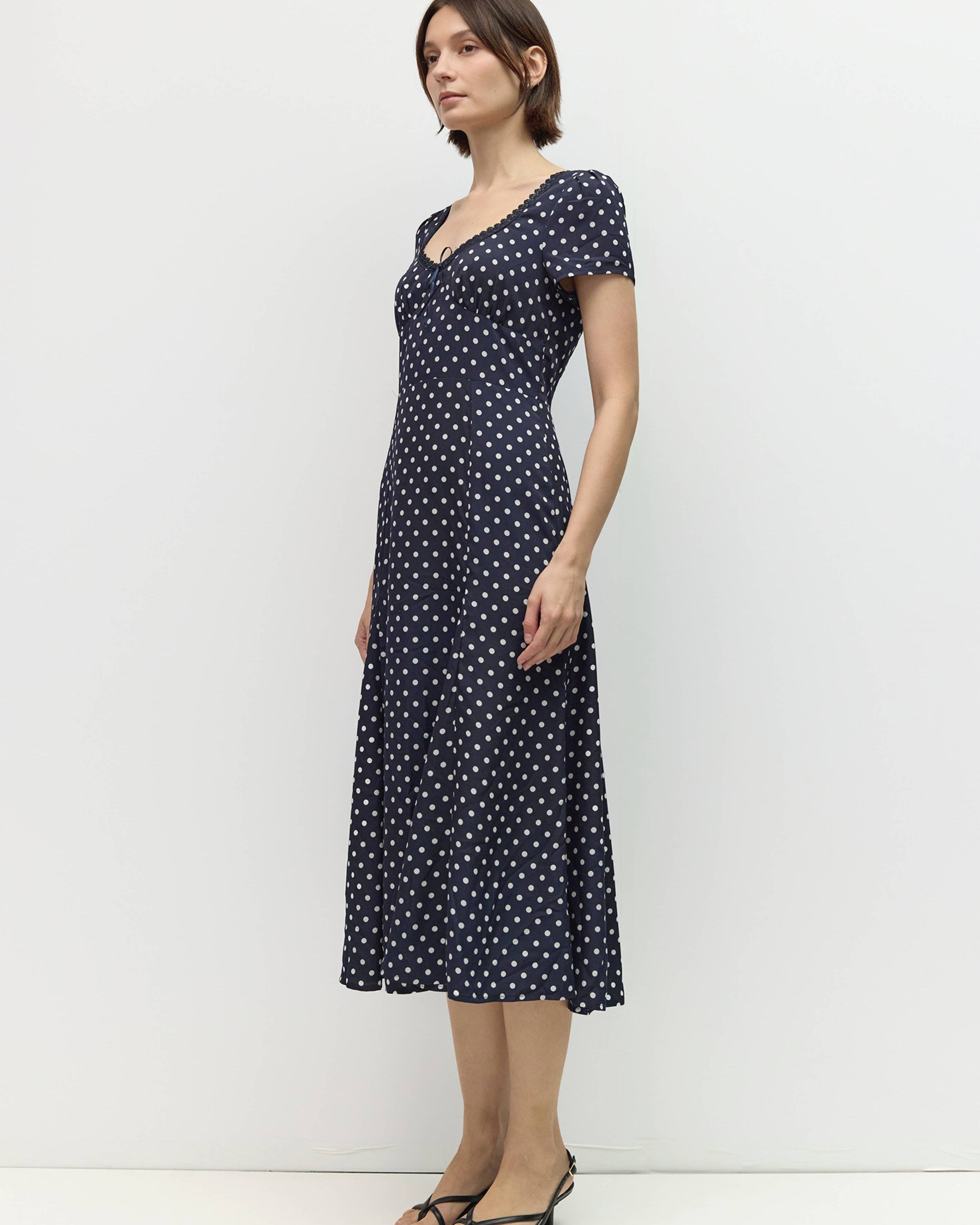Woman wearing a navy dress with white polka dots against a white background