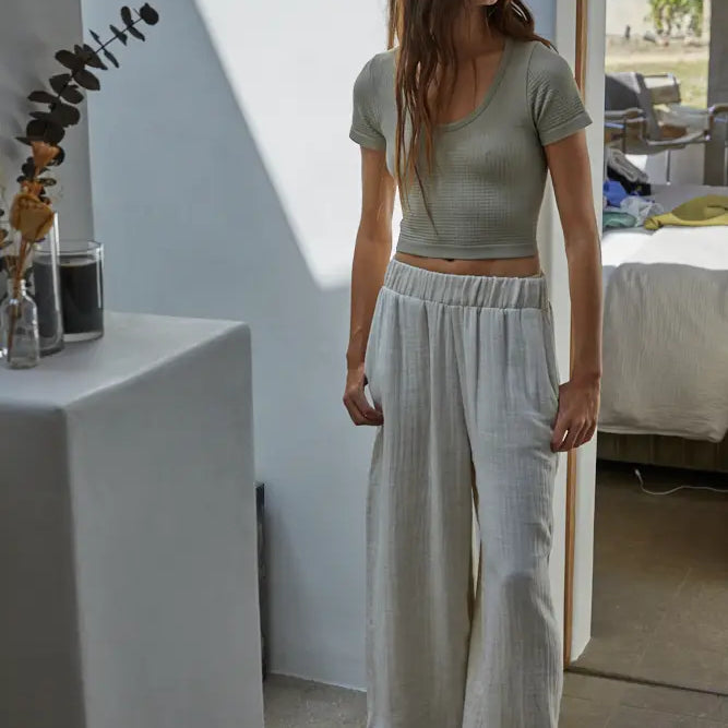 Woman wearing a green top and light gray pants standing in a room with a mirror.