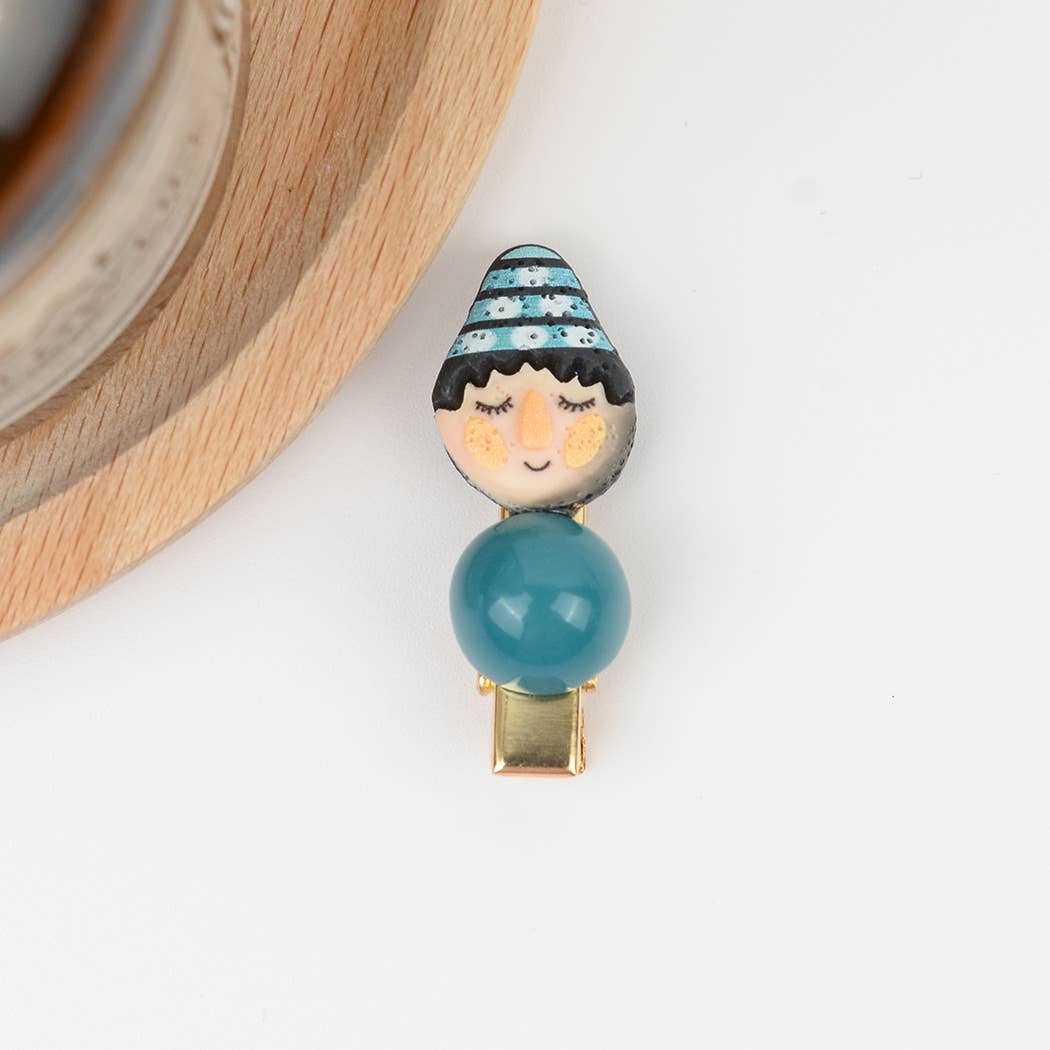 Hair clip with a face design and teal ball on a white background