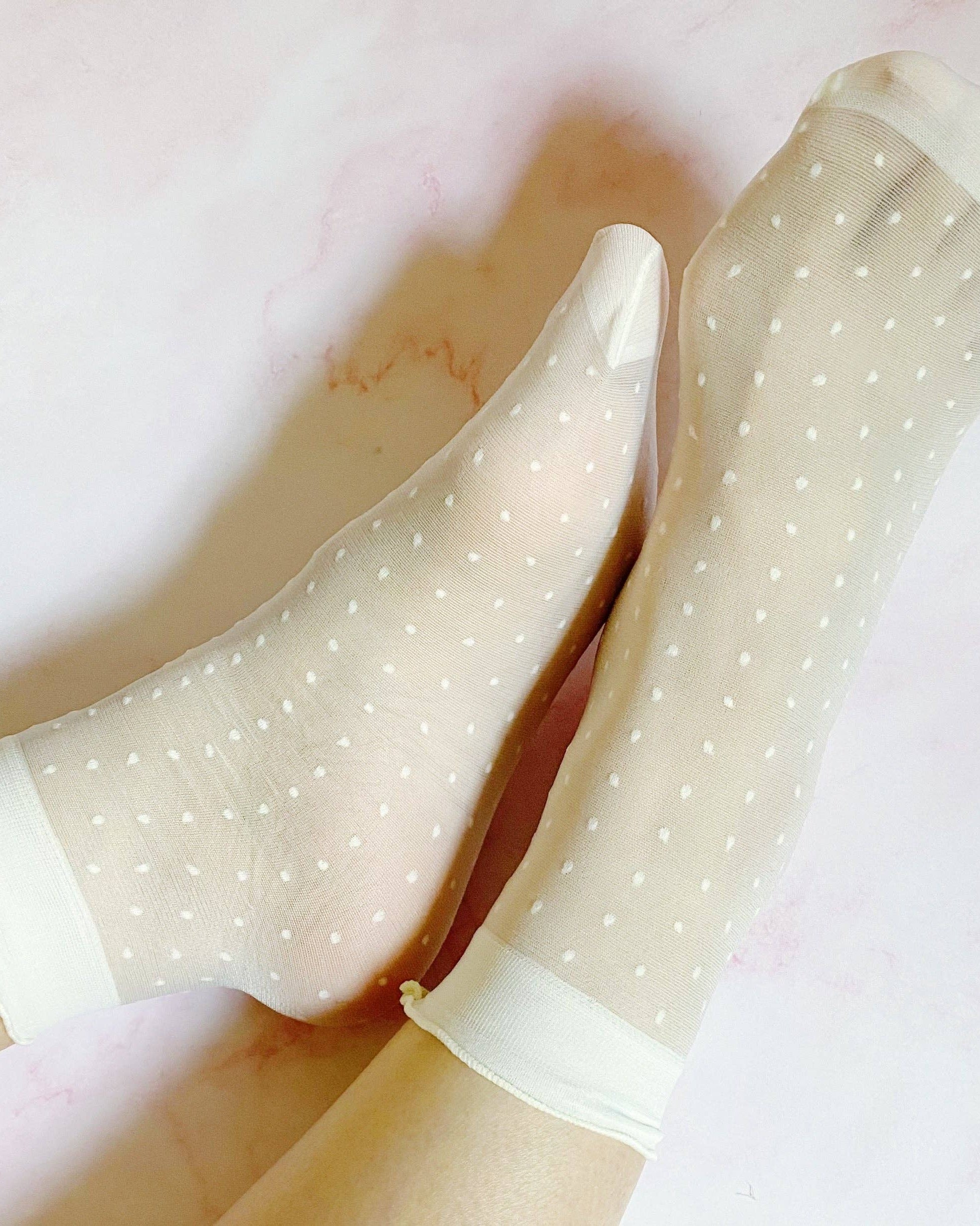 Sheer beige socks with white polka dots on a light pink background