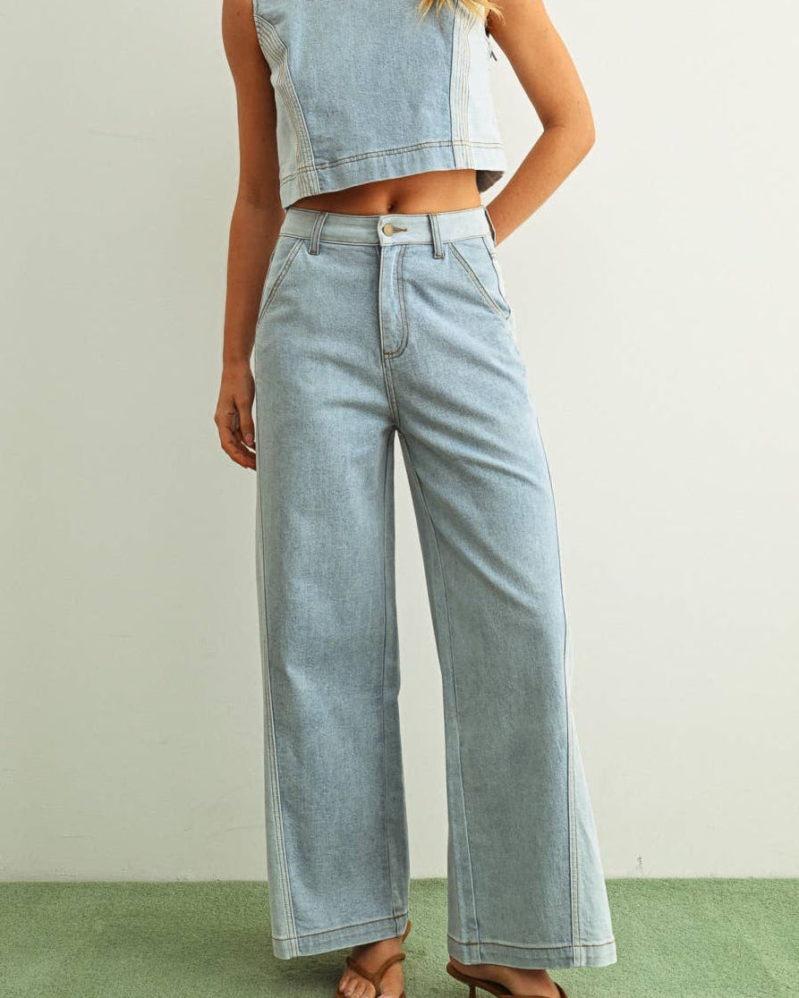 Woman wearing light denim jeans and light denim top standing behind a white background