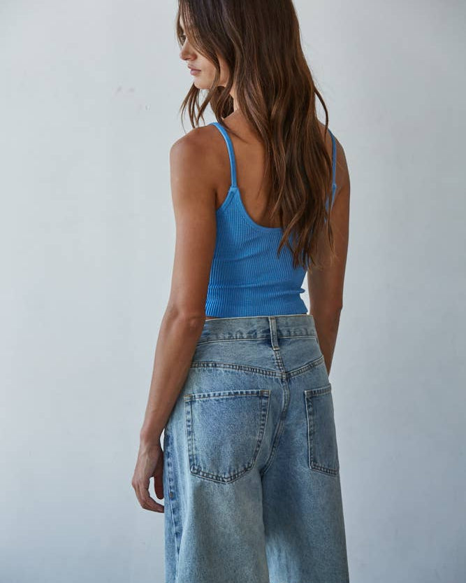 Woman wearing a blue tank top and denim skirt against a plain background
