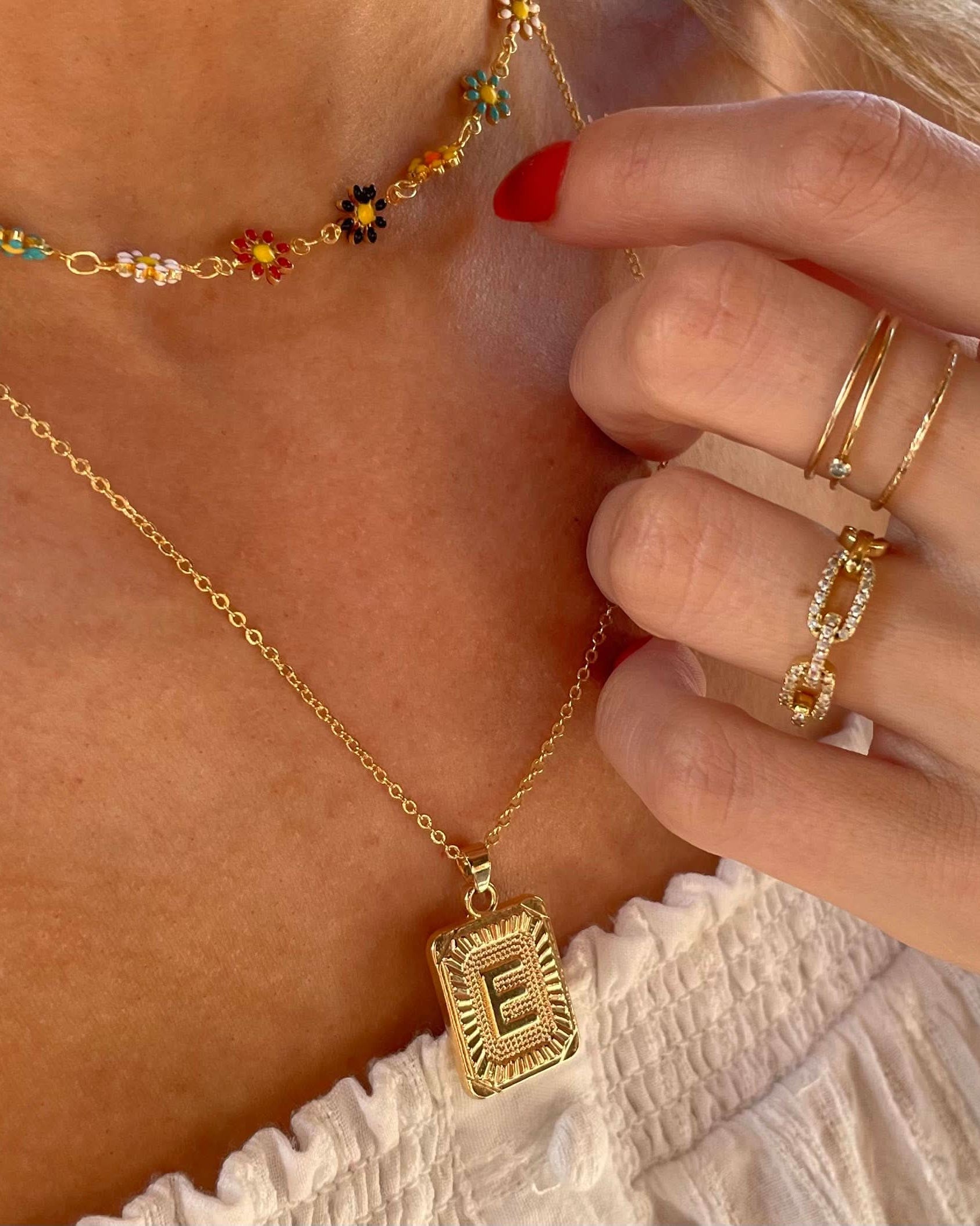 Woman wearing a letter E tarnish free gold initial charm necklace with a colorful flower necklace while wearing gold rings.