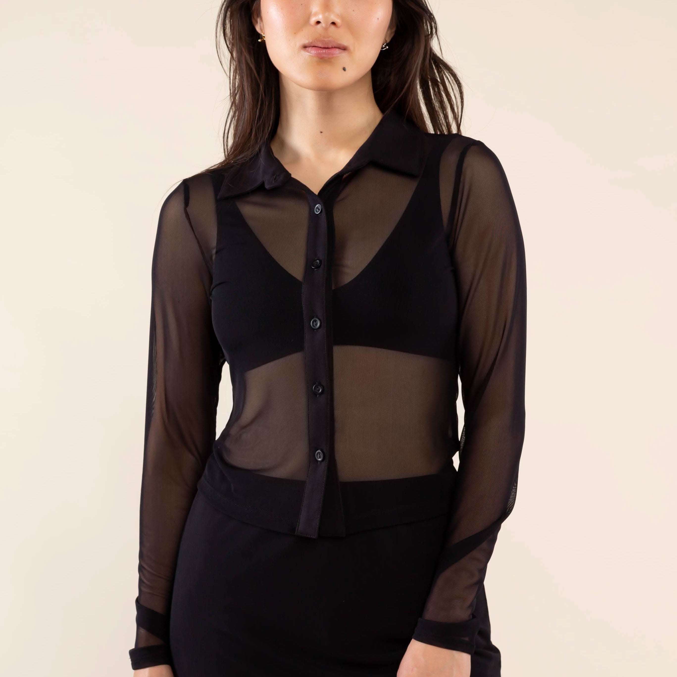 Woman wearing a black sheer blouse over a black dress against a plain background