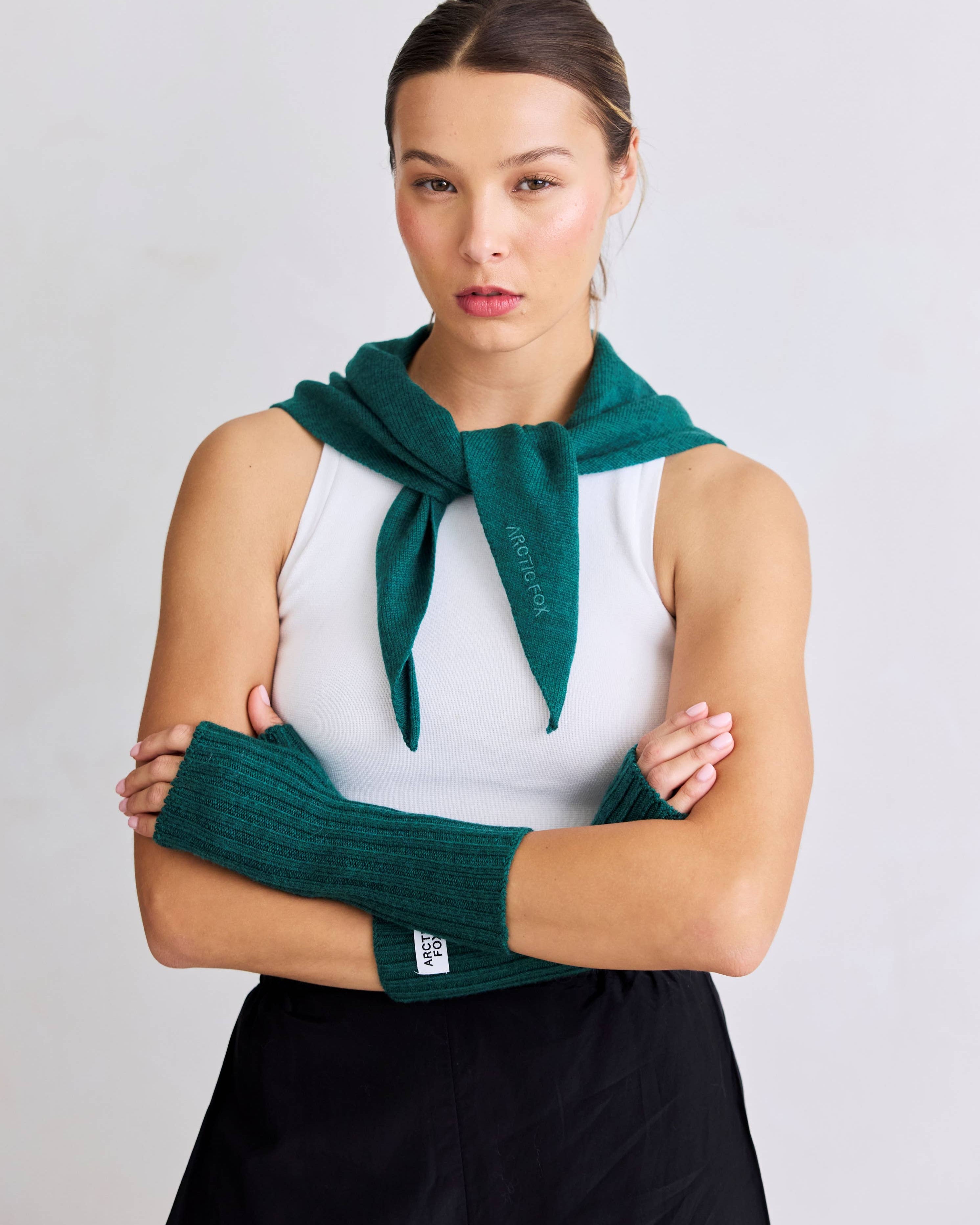 Woman wearing a green knitted scarf and arm warmers against a plain background