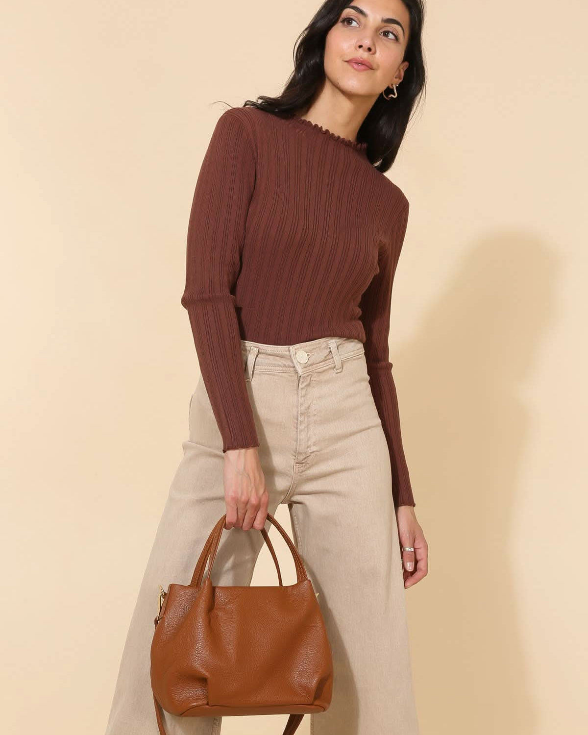 Model wearing plum red and beige carrying Big chestnut brown leather handbag purse with handles, strap, and gold details