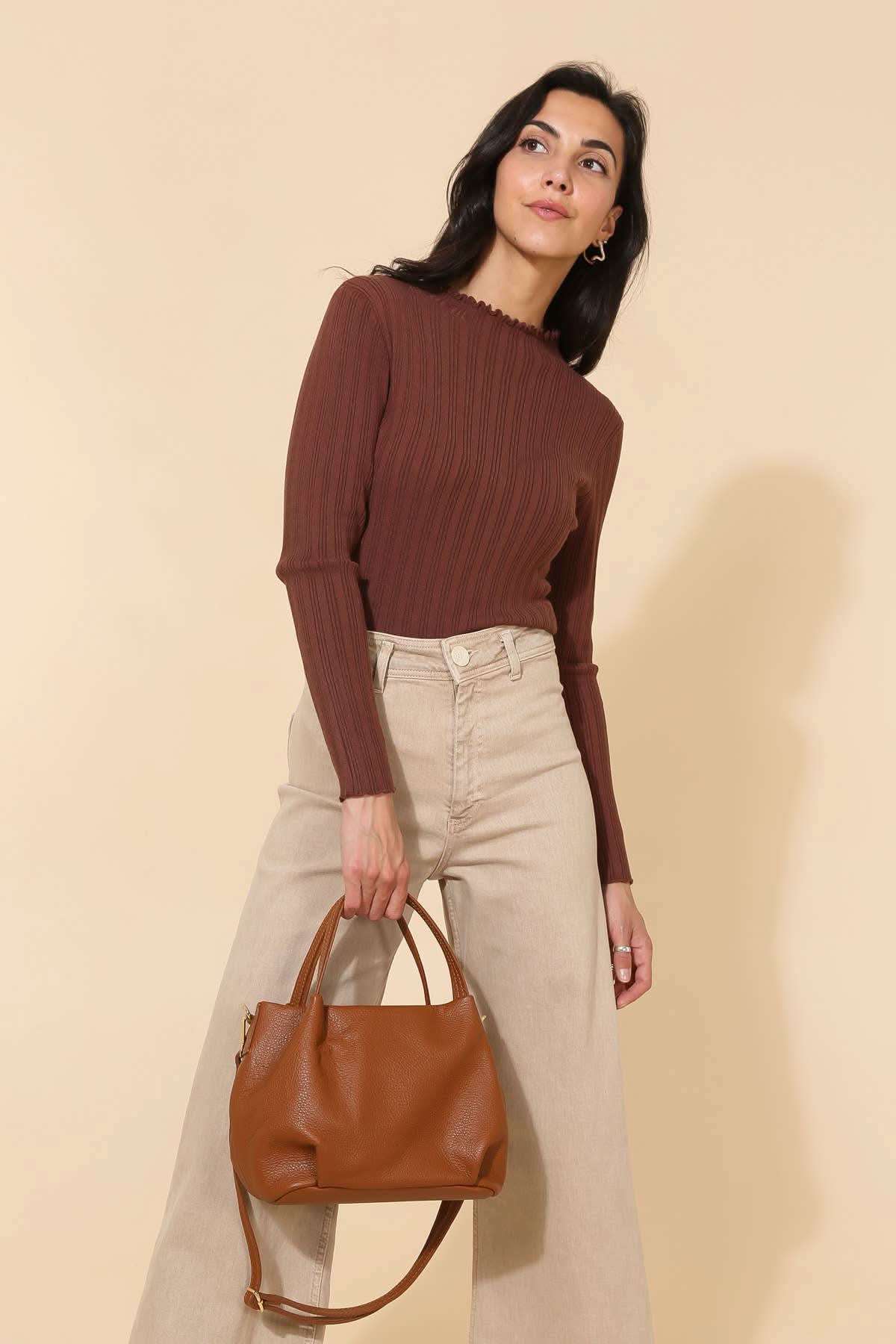 Model wearing plum red and beige carrying Big chestnut brown leather handbag purse with handles, strap, and gold details