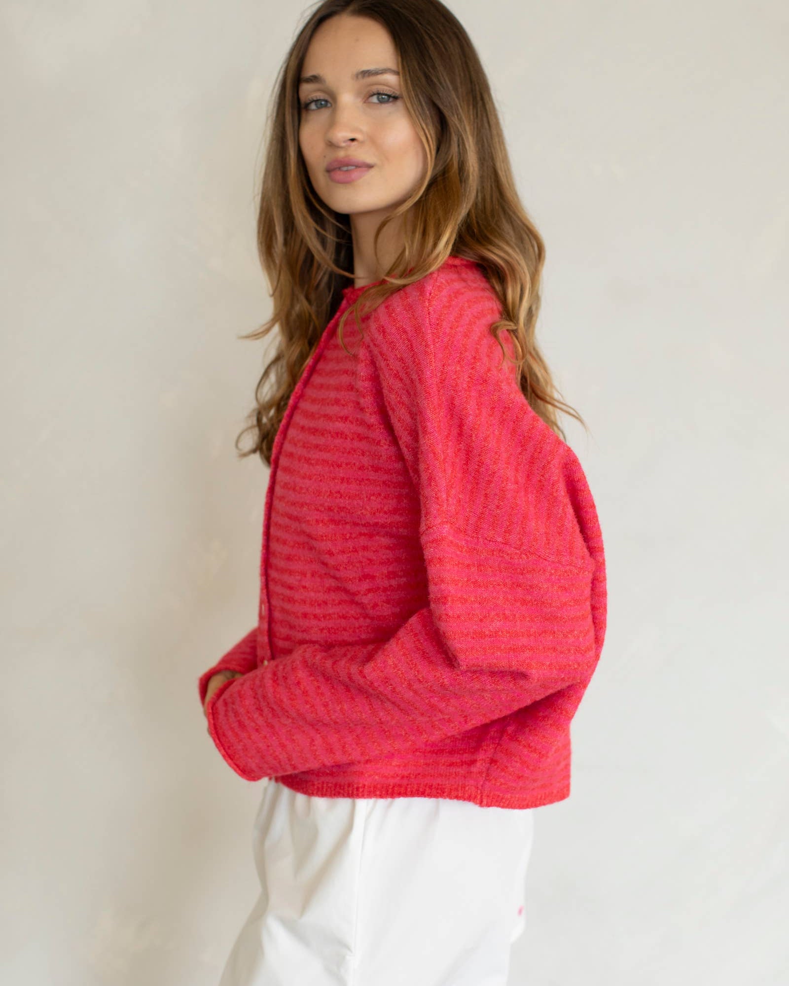 Woman wearing a red textured sweater and white shorts with a light background