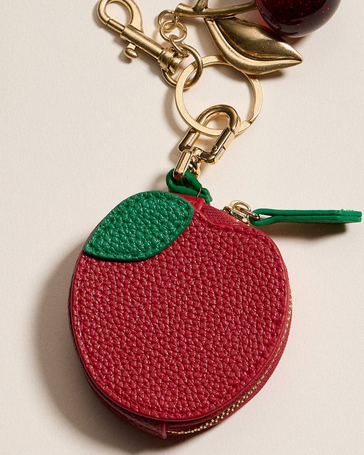 Red apple-shaped keychain with a green top on a beige background