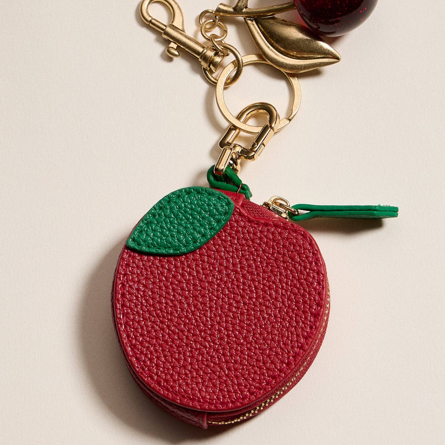Red apple-shaped keychain with a green top on a beige background
