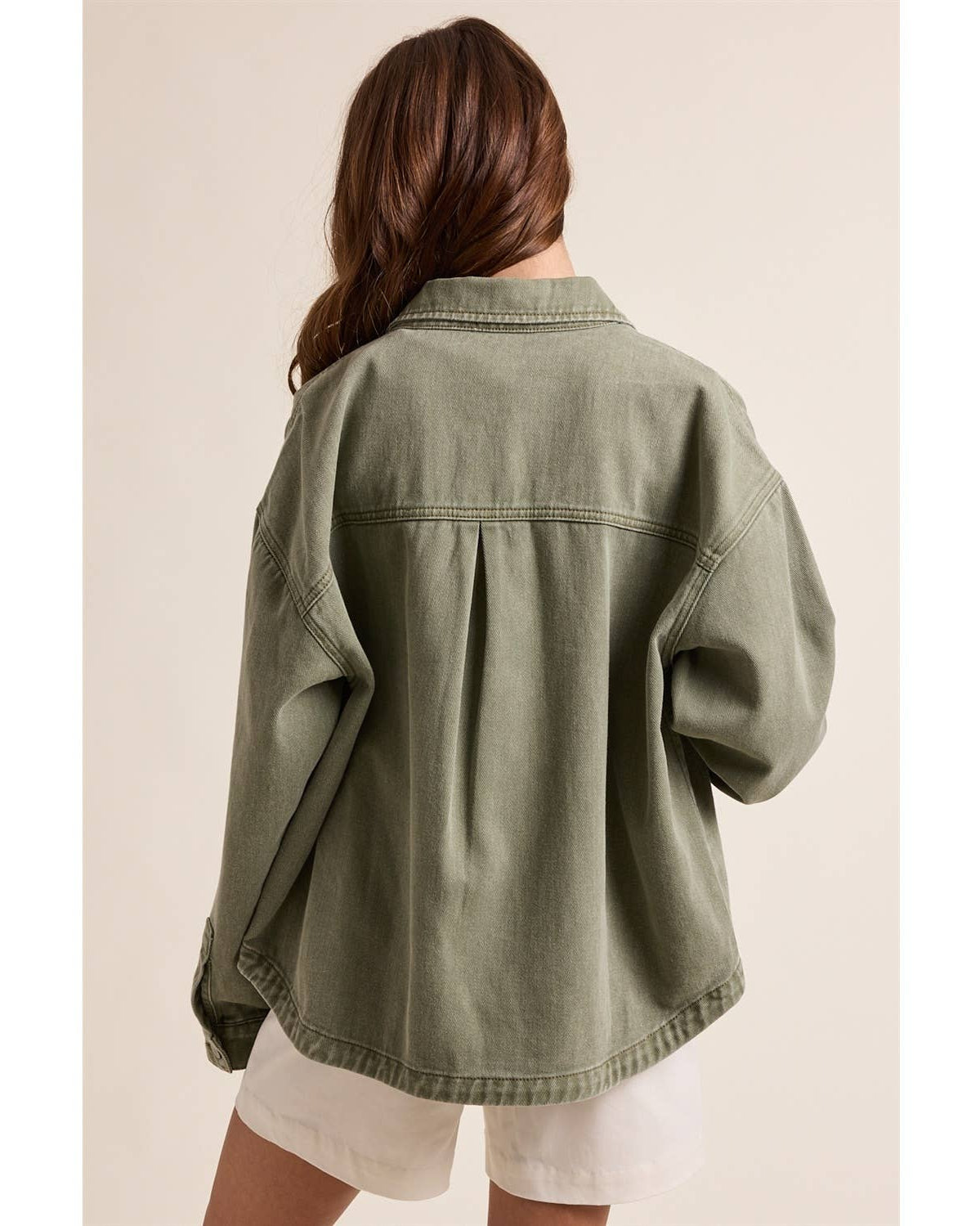 Person wearing a green denim jacket on a beige background