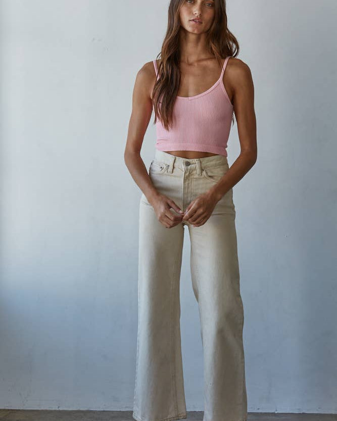 Woman wearing a pink tank top and beige pants against a plain background