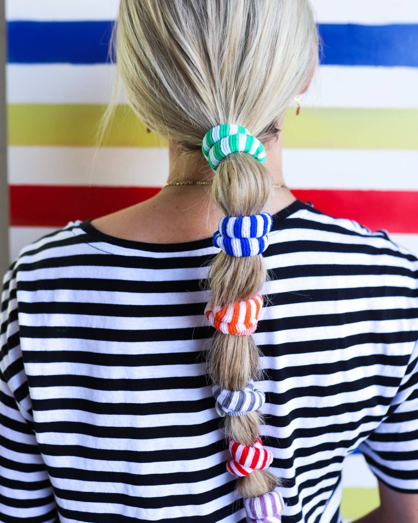 Person with colorful hair ties in a striped shirt against a striped background