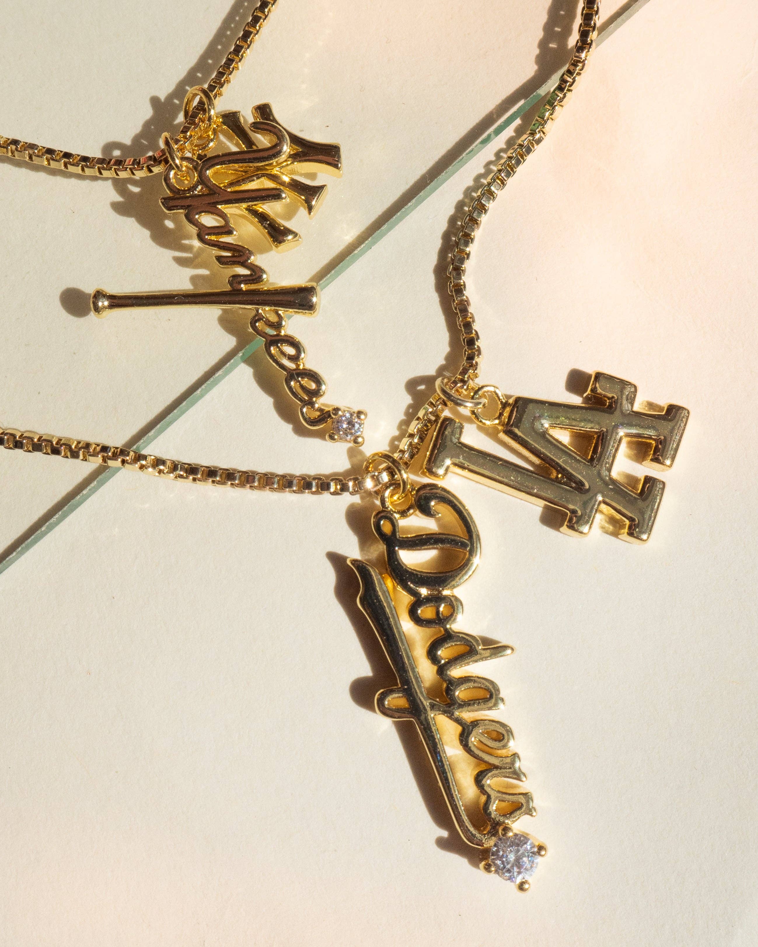 Gold necklaces with 'Dodgers' and 'LA' charms on a light background