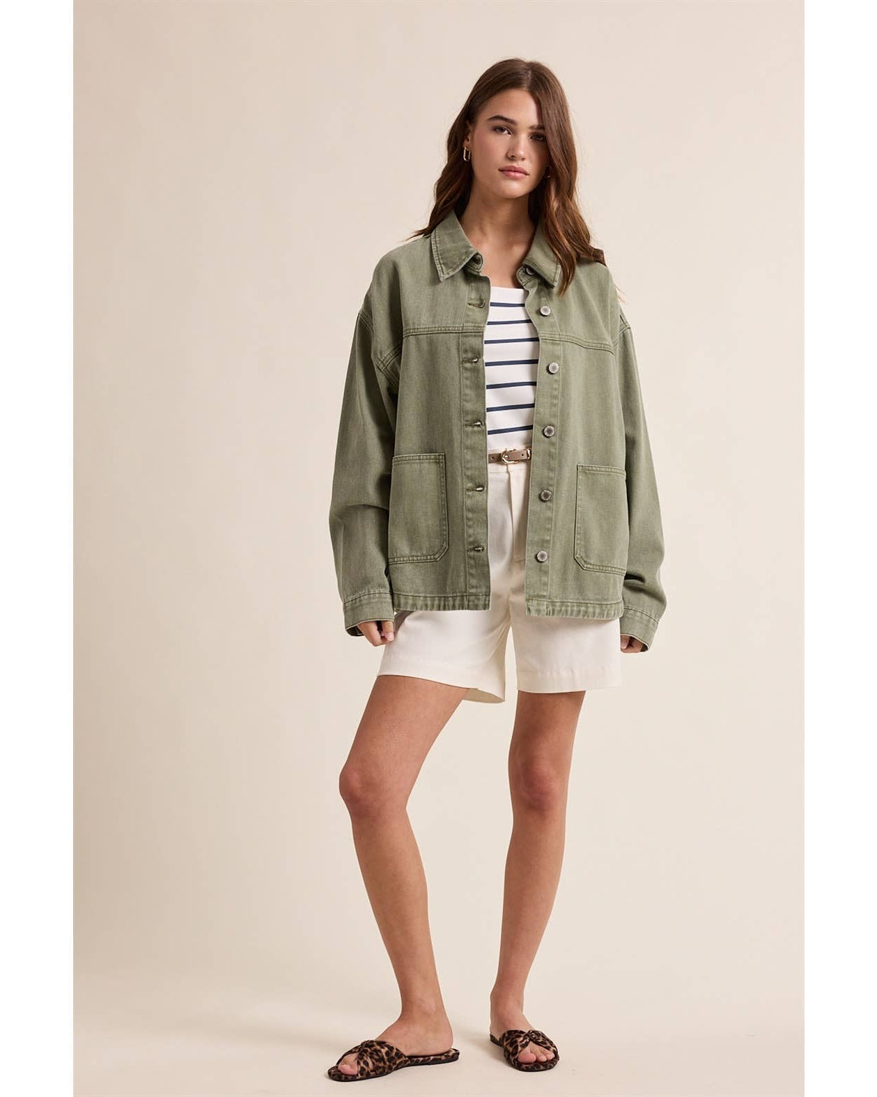 Woman wearing a green jacket, striped shirt, and white shorts on a beige background