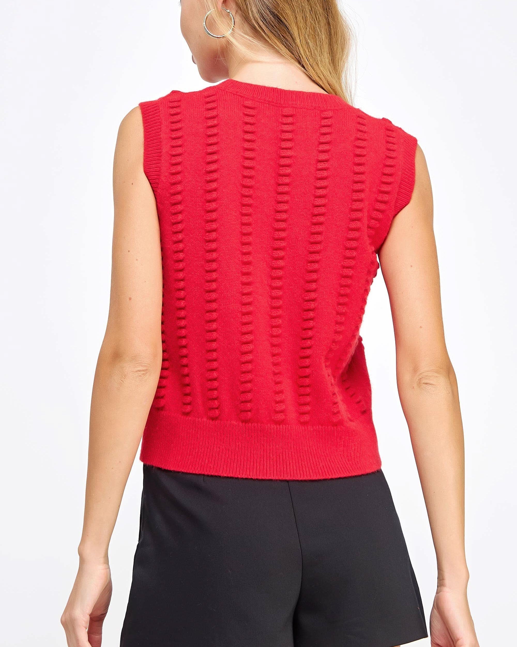 Woman wearing red textured sweater vest with black shorts