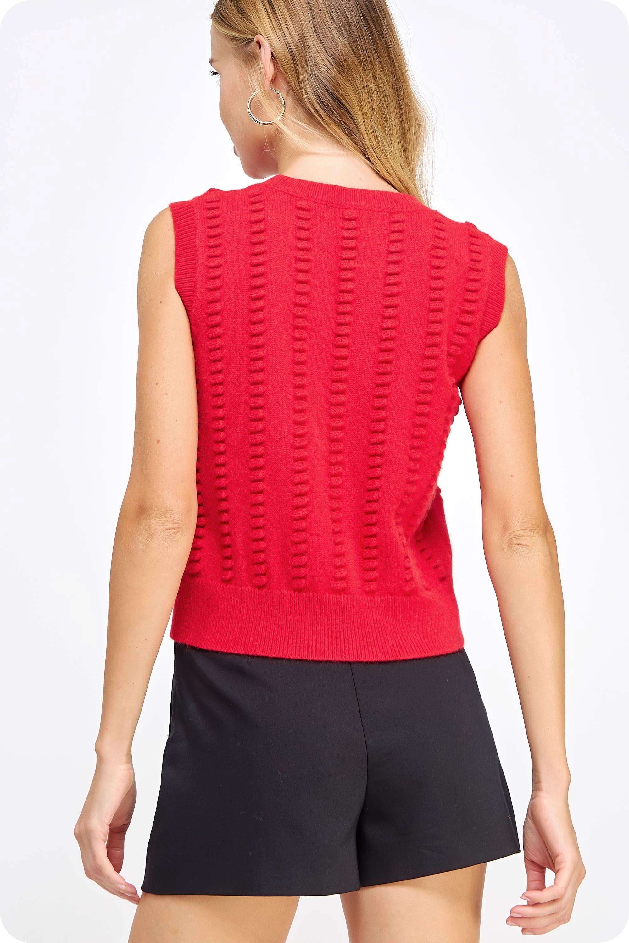 Woman wearing red textured sweater vest with black shorts