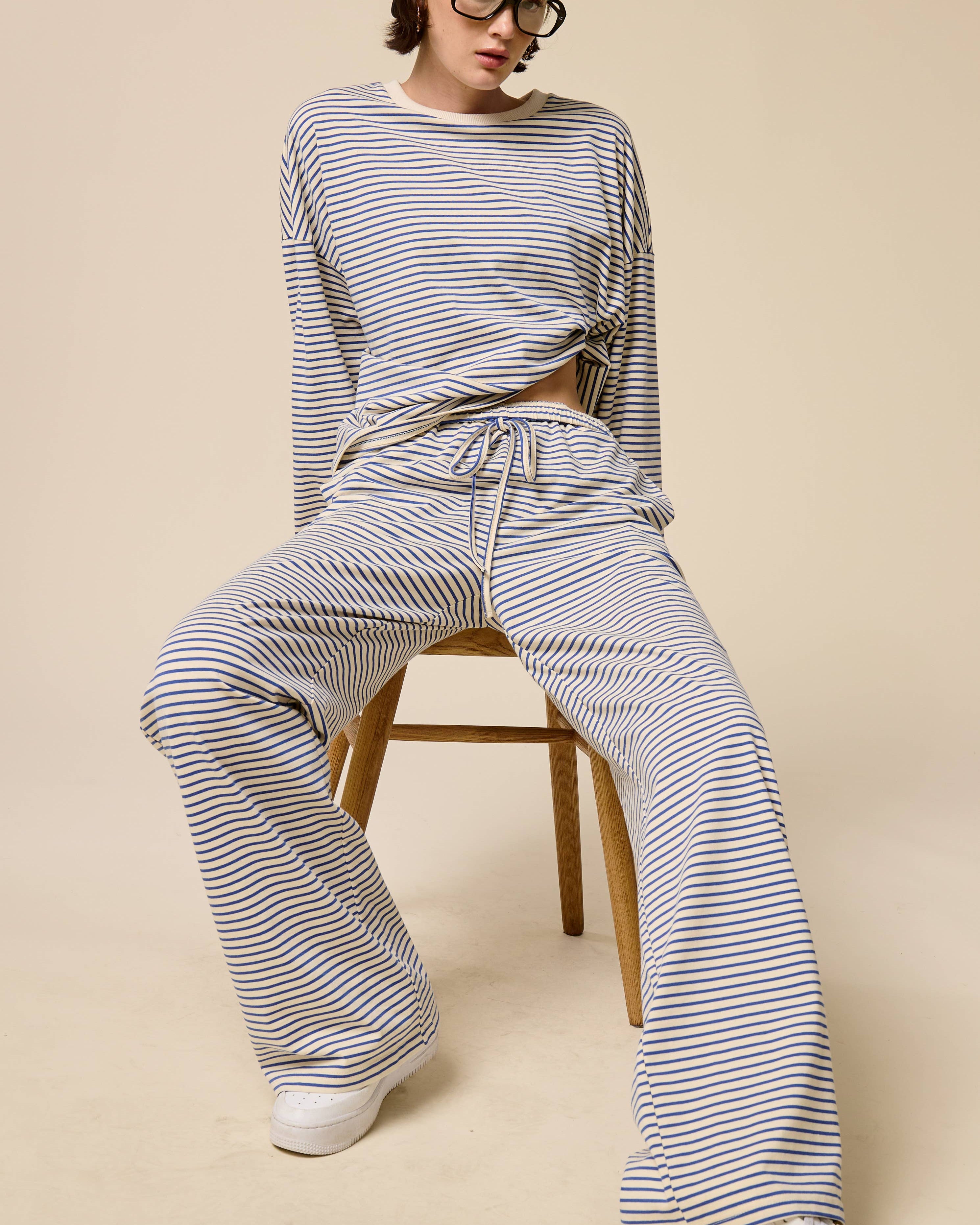 Person wearing a striped outfit sitting on a chair against a beige background
