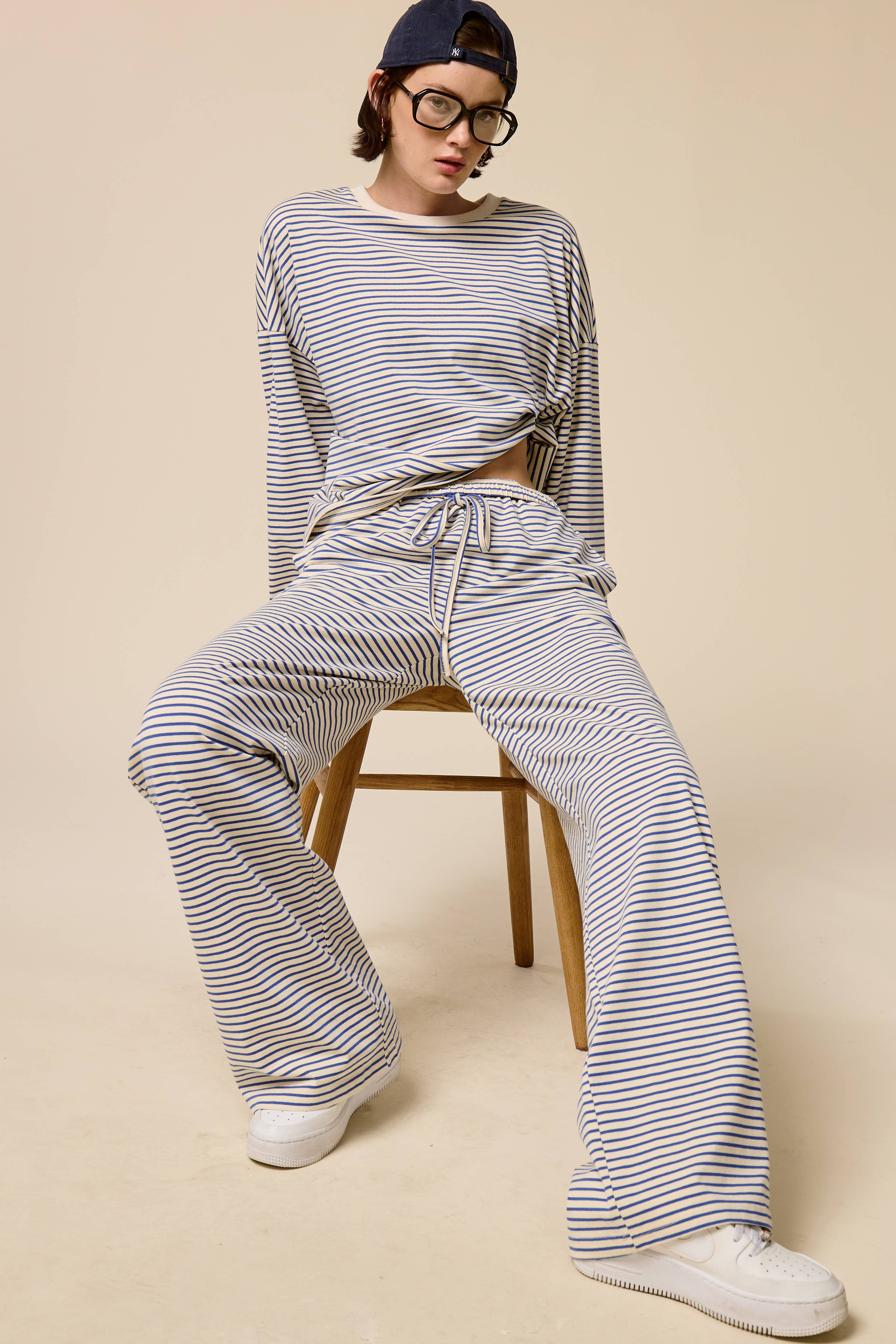 Person wearing a striped outfit sitting on a chair against a beige background