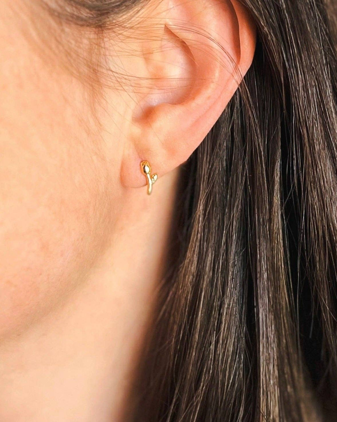 Close-up of an ear wearing a gold earring with hair partially obscuring the view.