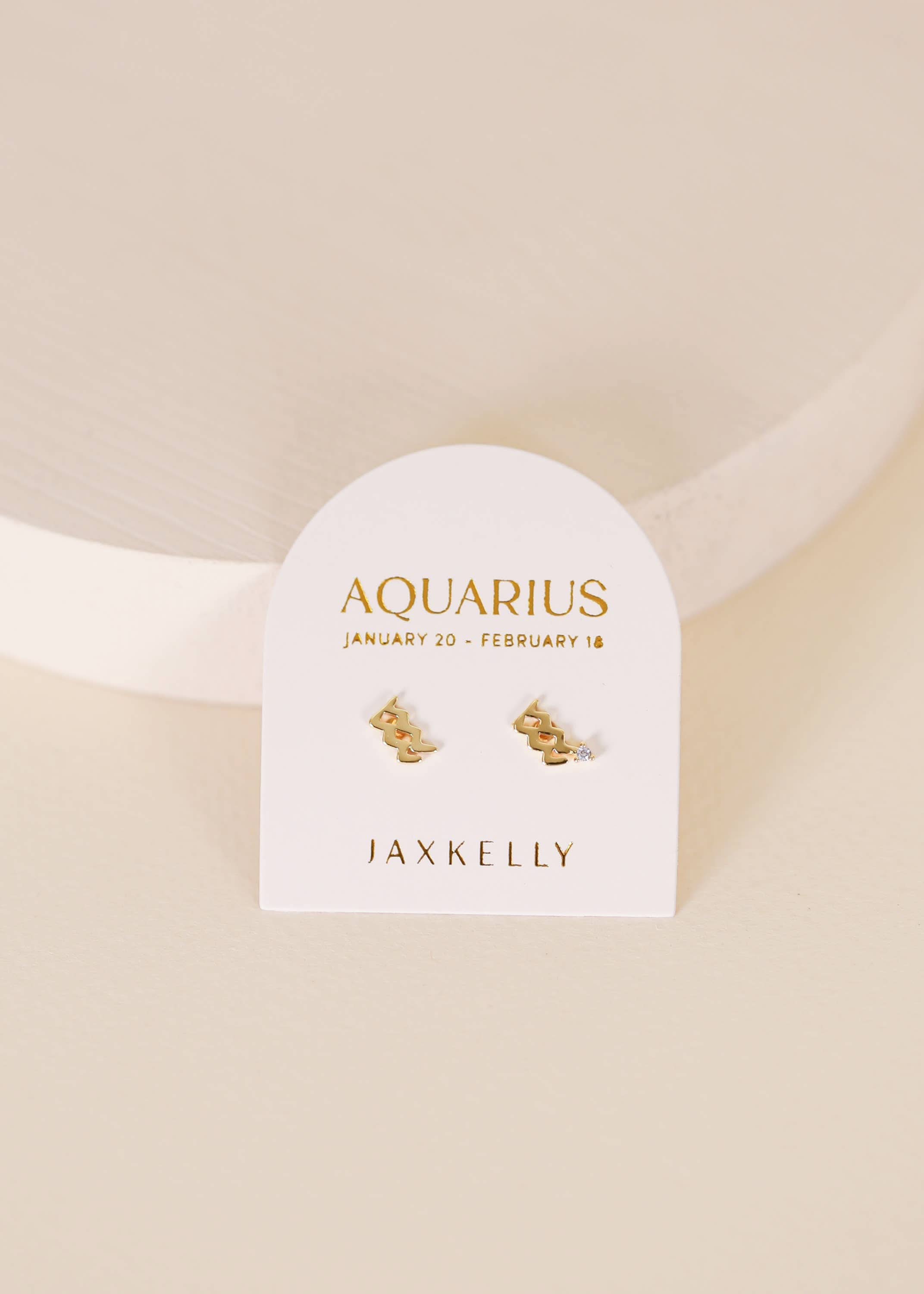 Gold zodiac charm studs in the shape of Aquarius astrological sign displayed on earring card