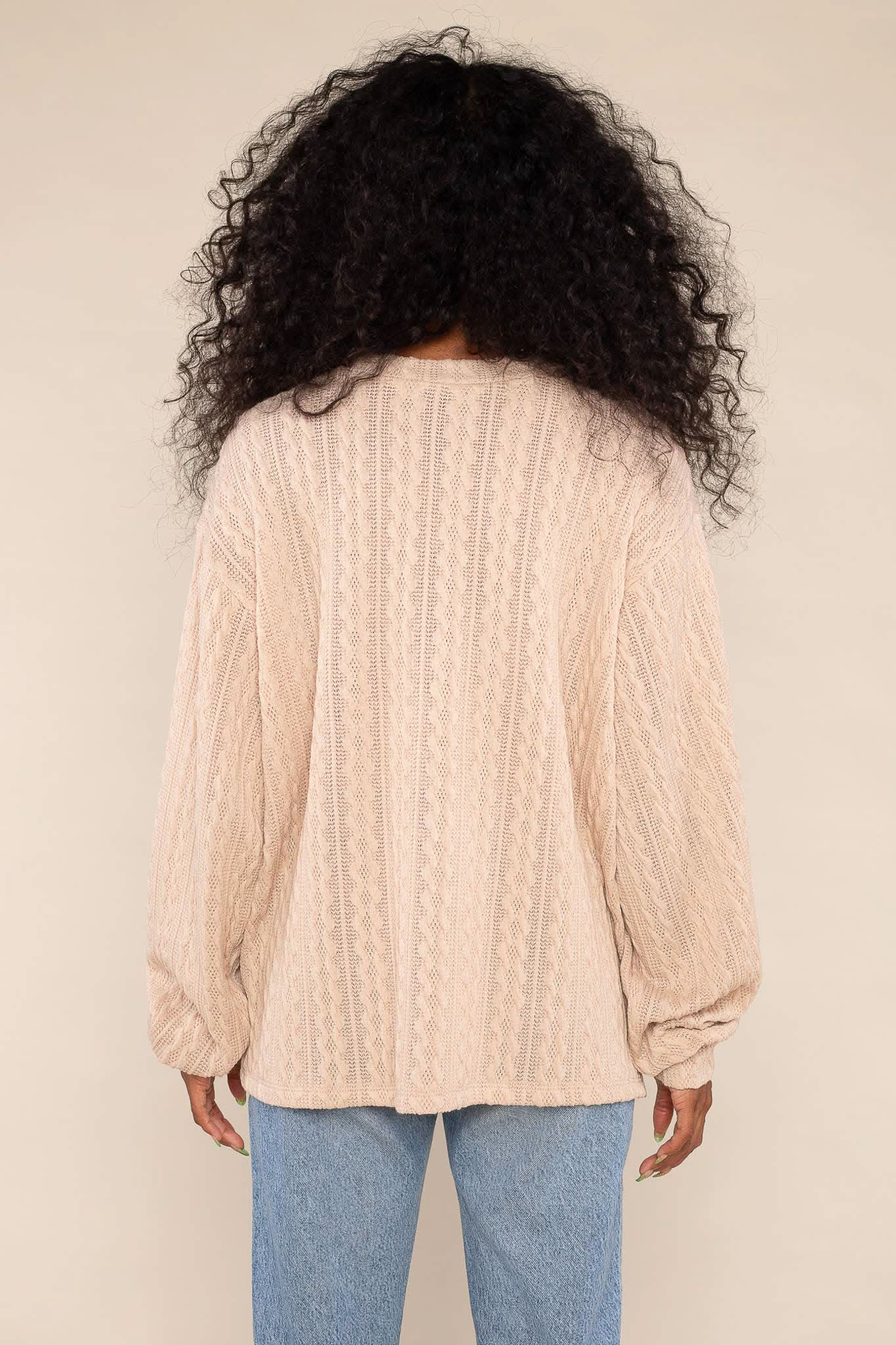 Woman wearing lightweight, beige, cable knit detail, sweater/ sweatshirt and blue jeans