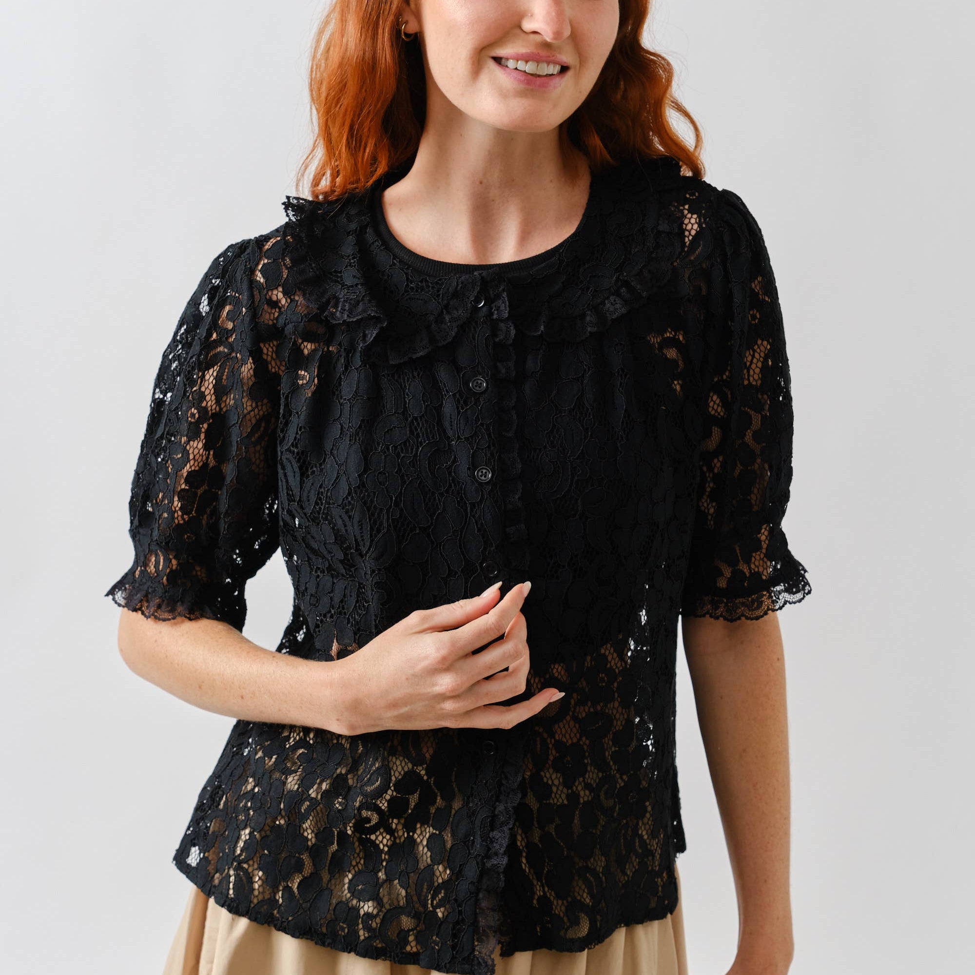 Woman wearing a black lace top and beige skirt against a white background