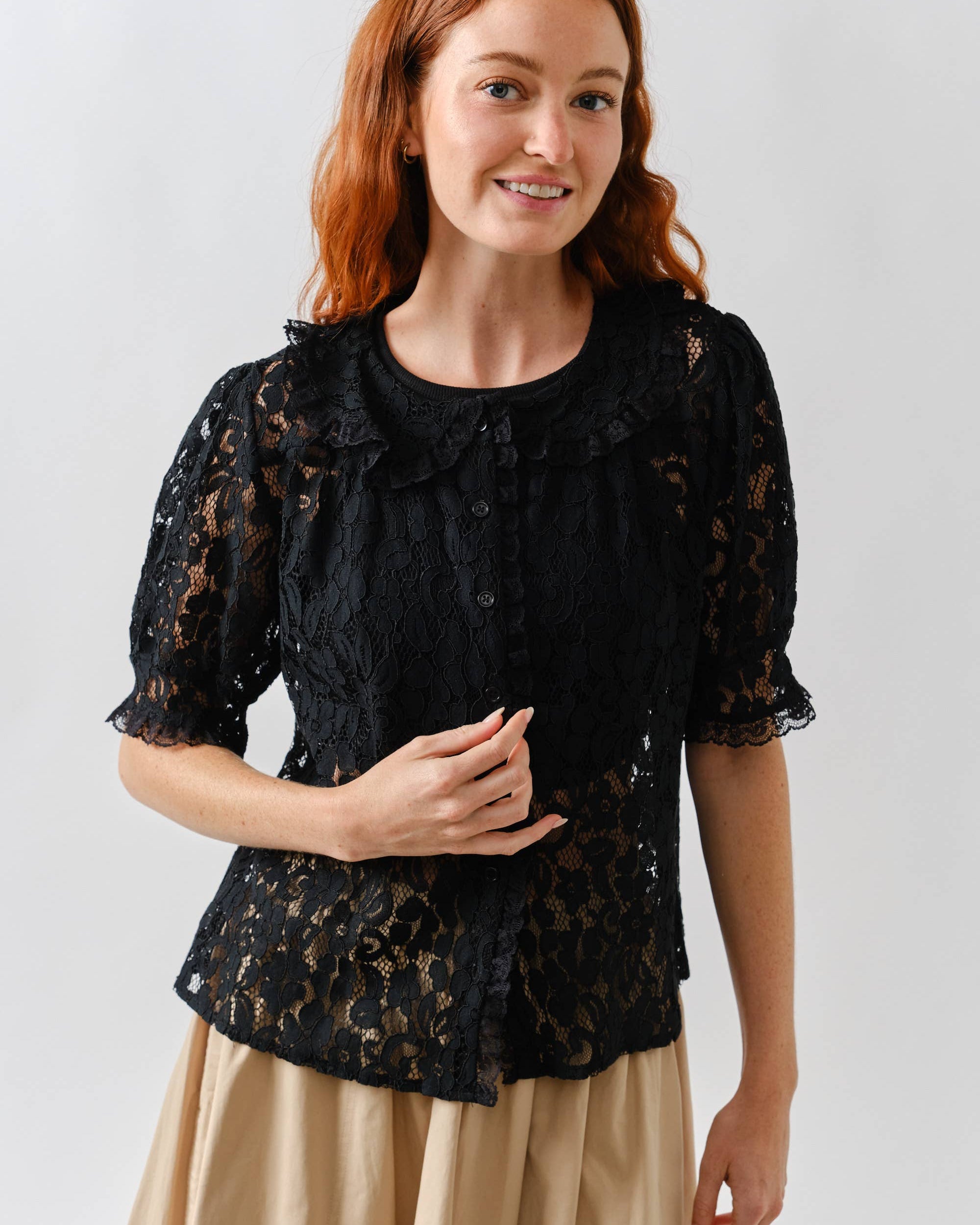 Woman wearing a black lace top and beige skirt against a white background