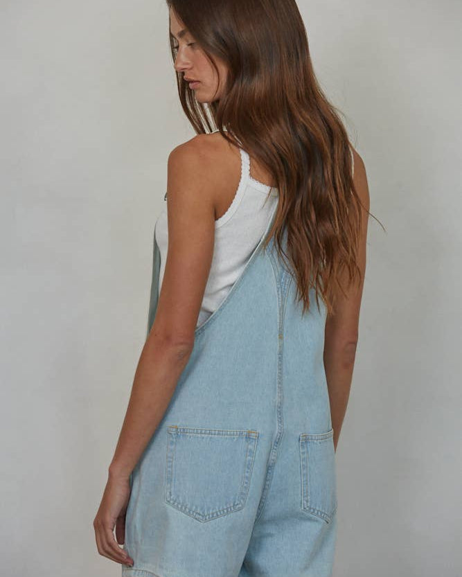 Woman wearing light blue denim overalls against a plain background